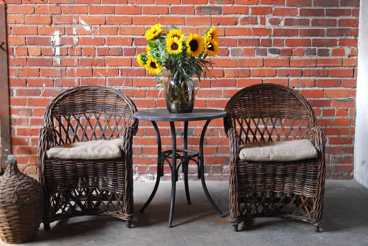 Organic pair of Bar Harbor style woven rattan twig armchairs constructed from natural rattan frames with graceful sweeping arms and back. Features an open fretwork back and apron. Upholstered with thin burlap seat cushions.