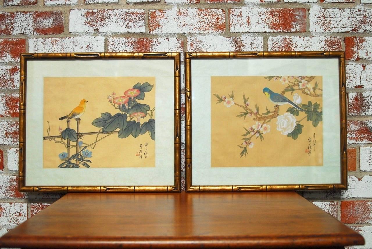 Pair of feminine chinoiserie style bird paintings. This lovely pair features hand-painted birds, flowers, and foliage on silk in calming colors with giltwood faux bamboo frames. The designs are reminiscent of hand-painted Degournay wallpaper