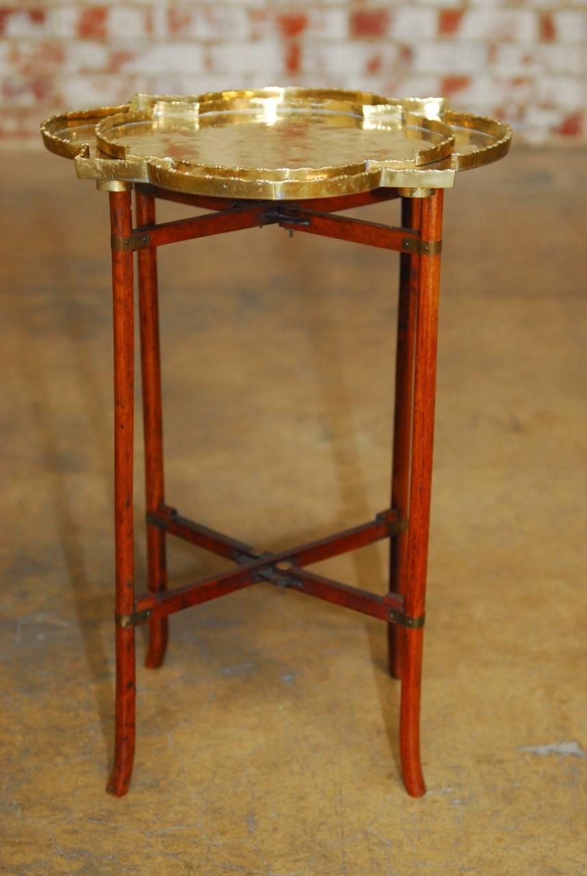 Stylish Asian folding leg brass quatrefoil tray table or drinks table with a matching serving tray. Features a delicate four-leg folding wooden base supporting a quatrefoil shaped incised brass tray with a conforming smaller tray inside. Each tray