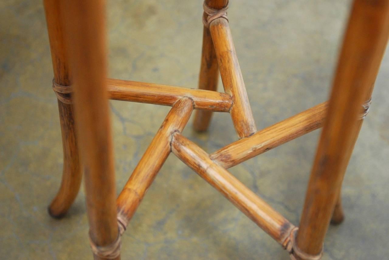 Organic pair of Mid-Century Modern bamboo rattan plant stands by McGuire Furniture Company. Each tall Stand is constructed with five straight legs having splayed feet and joined together using rawhide leather strapping. The two stretchers are