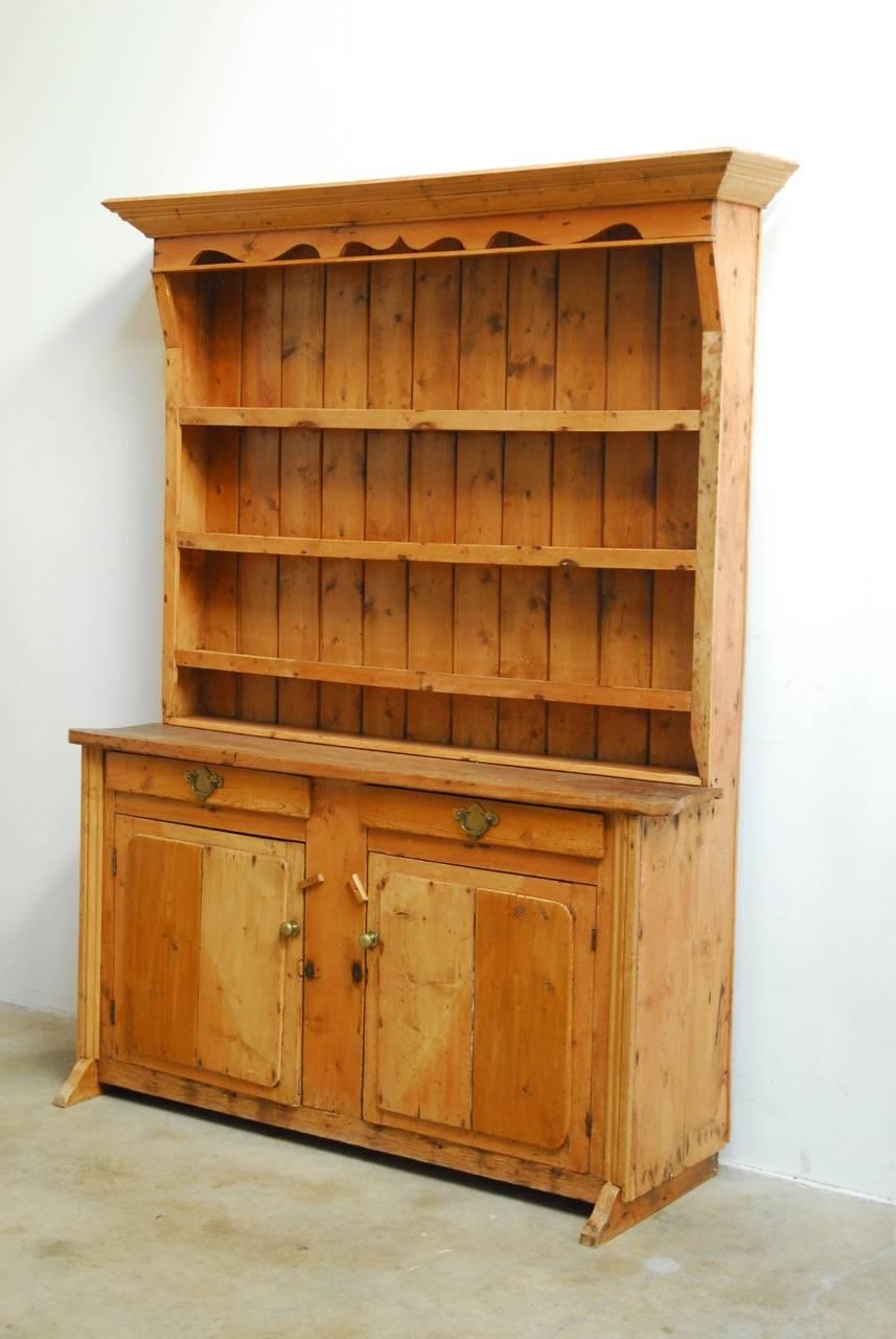 Rustic 19th century English pine welsh cupboard dresser with plate rack display. Beautiful distressed antique finish on the natural pine. Fronted by a case having two drawers, and two storage doors. Topped with a three-shelf plate rack featuring a