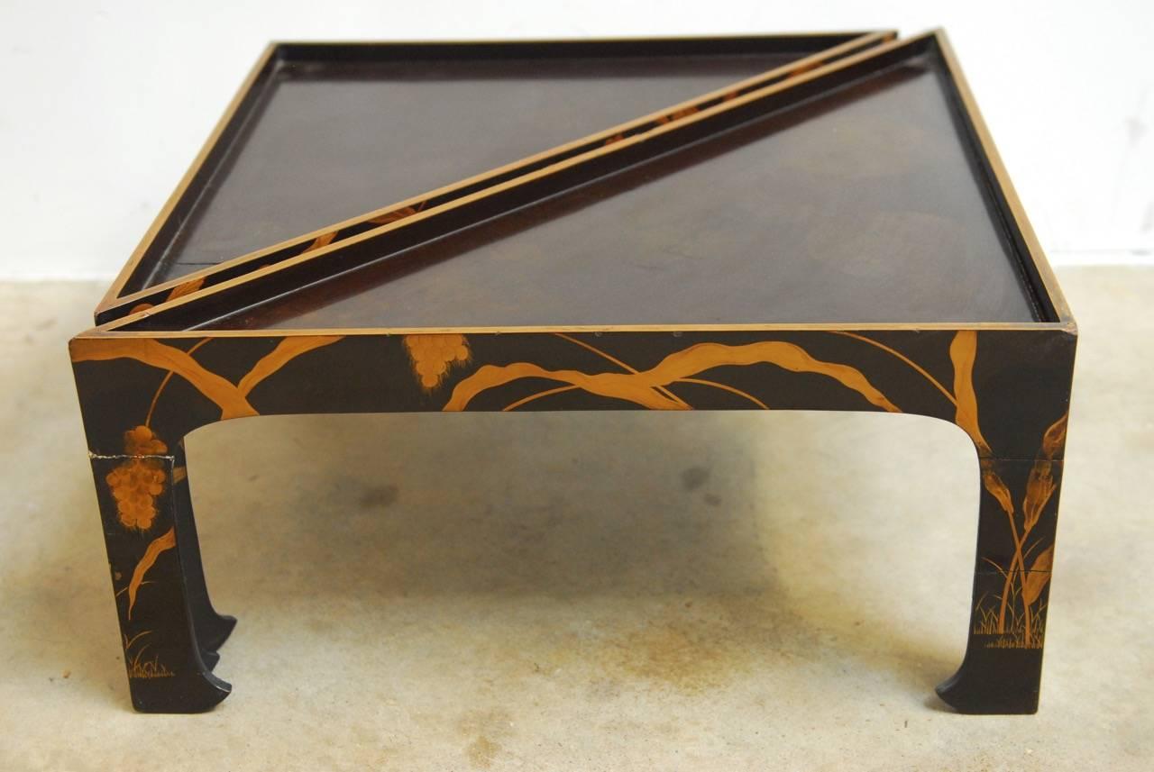 Fantastic nest of four chinoiserie style lacquered stacking tray tables featuring a japanned gilt finish. Each triangular table is graduated in size and decorated with hand-painted birds and grasses. The tops of the trays are galleried and they are