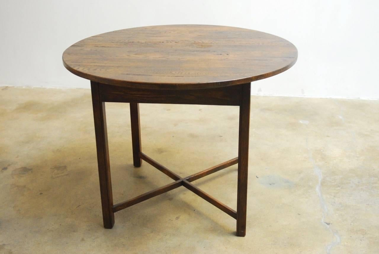Rustic 19th century English oak tavern table featuring a round plank top. The table is supported by four square skirted legs conjoined with an 