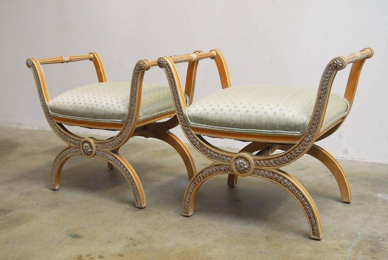 Classic pair of Italian X-form Curule benches or stools made in the neoclassical taste. Featuring relief carved scroll designs with rosettes on the ends of the stretchers. Upholstered in a brocade fabric with a quatrefoil motif. Generous seat pads