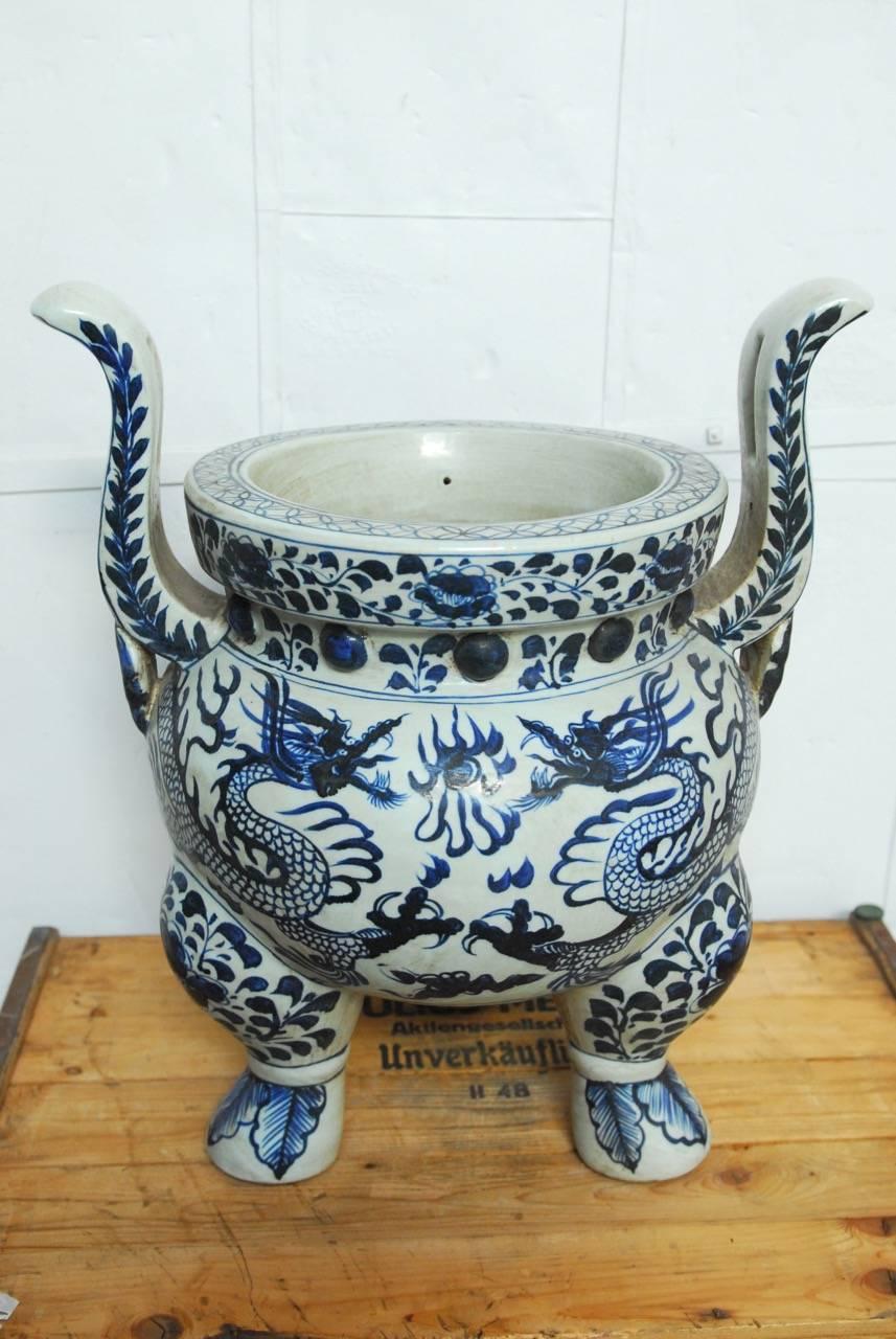 Rare monumental Chinese blue and white ceramic tripod dragon censer. Features a large ding form with two large flying dragons. Made in the Qianlong period style with three short legs, a thick rim, and arms all decorated with foliate and scrolling