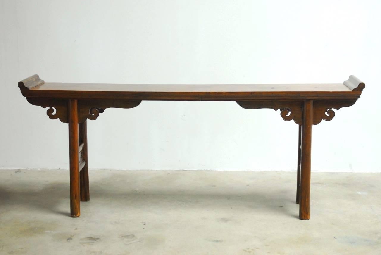 Splendid 19th century Chinese altar table or console table constructed from elm. Features a 2 inch thick solid elm top panel with scrolled ends and decorated with Ruyi cloud design spandrels. The console table is supported by massive round legs with