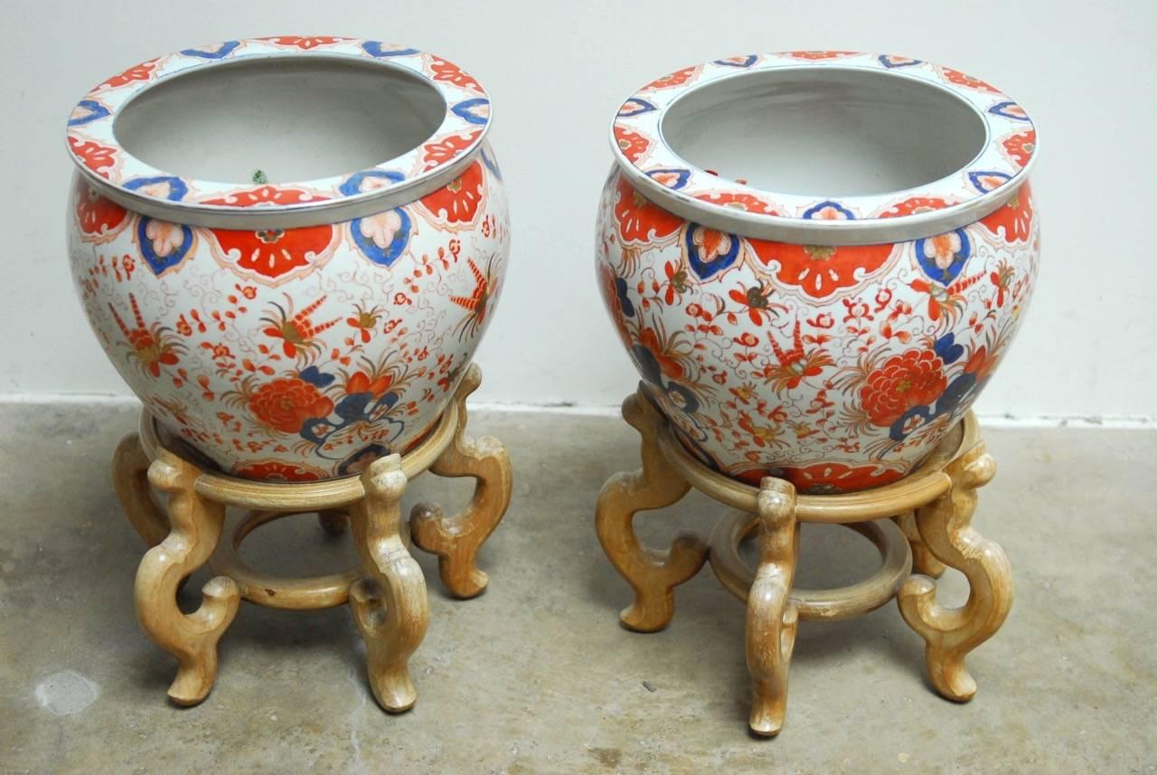 Remarkable pair of Chinese porcelain fish bowls on hardwood stands made for Gumps department store. Featuring a brightly colored body of orange and blue decorated with a flowering vine motif over a white background. These large urns measure 12