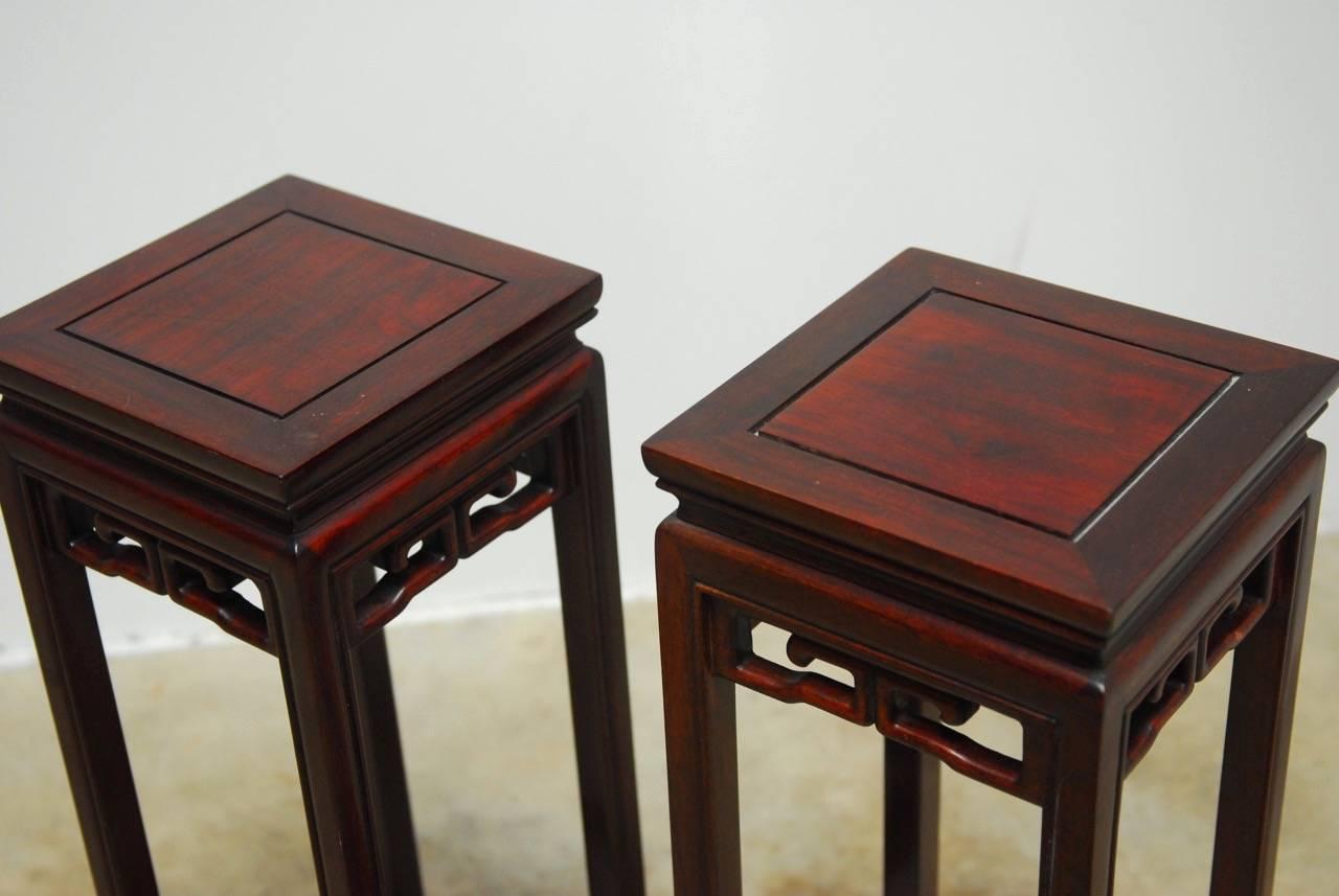 Handsome pair of Chinese carved Rosewood plant stands or pedestal tables. Featuring a square floating top panel and decorative Greek key motif aprons. Supported by long square legs conjoined by a stretcher ending with hoof feet. Heavy and solid with