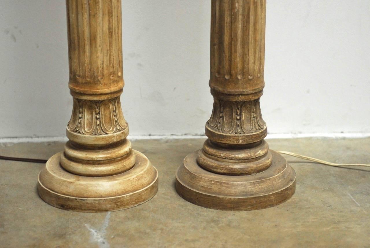 Elegant pair of Neoclassical carved wood columns made into floor lamps. Features a Greco-Roman doric style turned and fluted wood column with a beautifully distressed lacquer finish. Each lamp has a round base and brass vintage hardware with