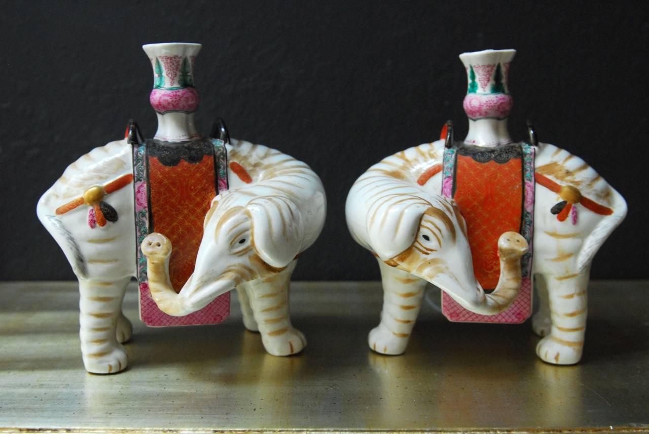 Exquisite set of four hand-painted porcelain elephant candleholders made by Mottahedeh. Each elephant is caparisoned with Asian motif saddles in rich colors and gilt. Two are looking left, and two right direction. Each is topped with a candlestick.
