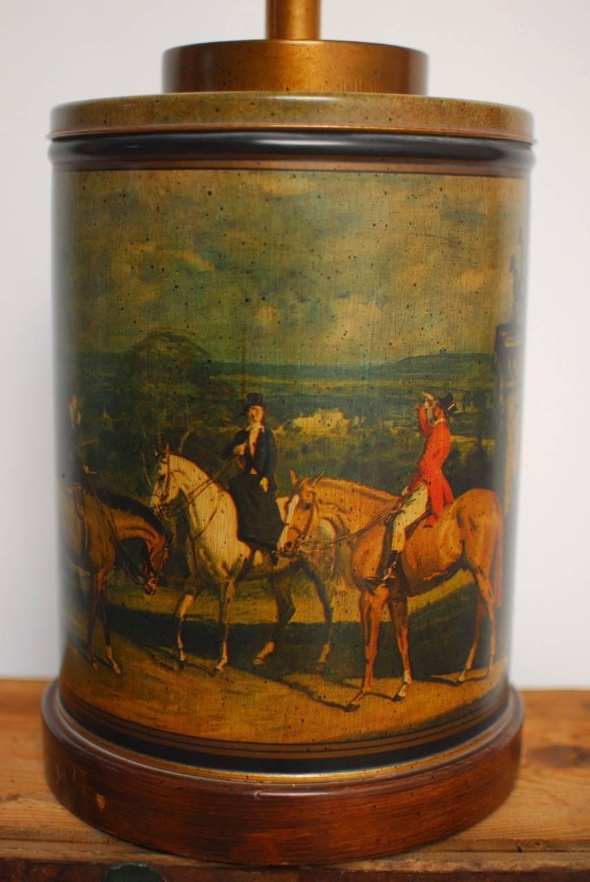 Charming Frederick Cooper equestrian tea canister table lamp featuring horsemen on a fox hunt. Round lamp in the form of a tea tin caddy with a lid mounted to a wooden base. Topped with brass hardware and a round metal ring finial.