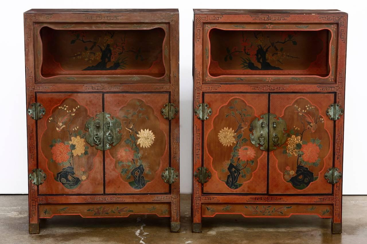 Stunning pair of Chinese red lacquer cabinets featuring an open shelf top design. Each cabinet is fronted by two doors that open to a two shelf interior. The cases are decorated with floral and fauna scenes featuring small birds and chrysanthemums