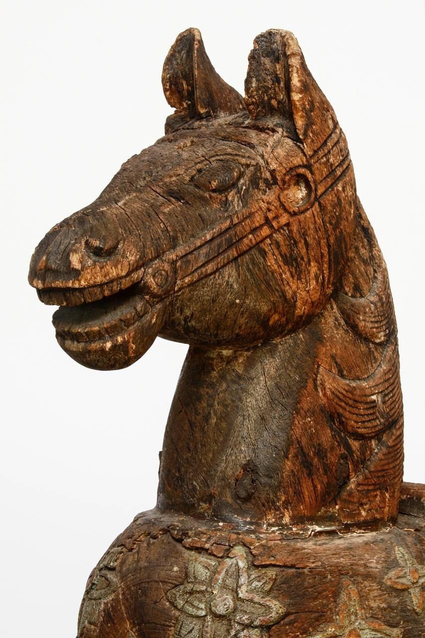 Charming carved wooden temple horse from India mounted on a wooden stand. Features an ornate distressed and faded polychrome finish of decorative carved flowers. Depicted standing with a saddle and bridle. Lovely wear and distressed finish.