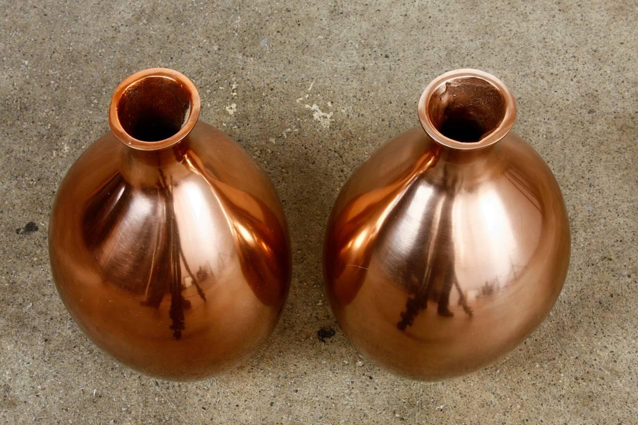 Artisan pair of Asian polished and hand-formed copper vases retailed by Gump's in San Francisco, CA. Thick solid copper vases feature a polished finish and slightly biomorphic form resembling studio pottery. The bulbous bodies have a narrow neck and