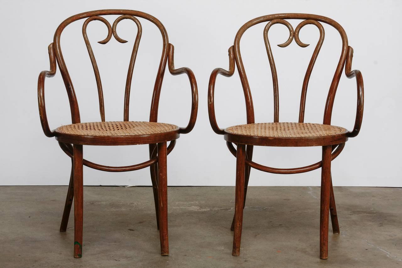 Pair of Thonet style bentwood and cane armchairs featuring beautifully sculpted arms and heart motif back splats. These cafe chairs have a rich, distressed finish and noticeable wear to the cane seats but are strong and stable. Original tags and