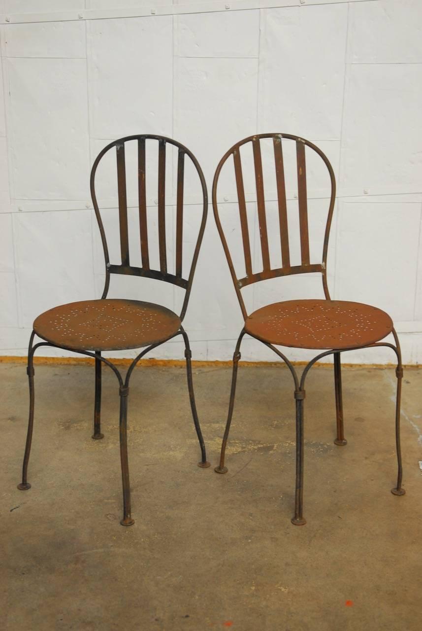 Classic pair of French iron bistro or cafe chairs constructed with a slat back. Features a round metal tubular frame with a round seat and decorative sunburst design. These make great garden chairs with a rich, distressed and patinated finish.