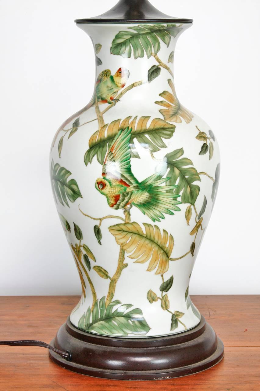 Posh pair of chinoiserie ginger jar form porcelain table lamps by Bradburn Gallery. Features an exotic decorated jar with palm banana leaves in a Beverly Hills Hotel style over a white ground among colorful parrots. The vase measures 14