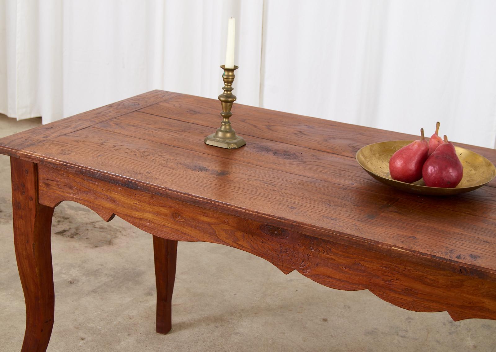 Rustic country French provincial farmhouse dining table or console table. The table is crafted from oak with a plank top having breadboard ends. The base has a storage drawer on one end and decorative scalloped aprons on the sides. Ample legroom