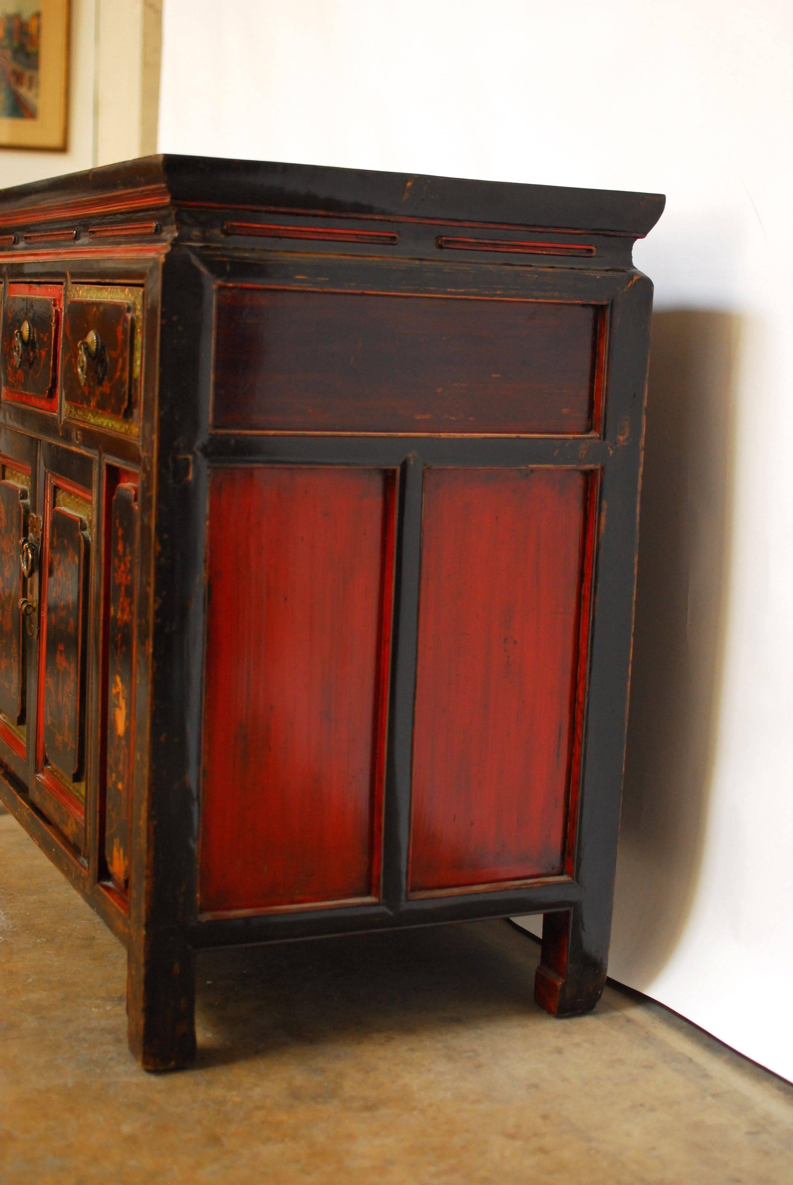 An antique, Chinese black and red lacquer sideboard buffet cabinet with a polychrome decorated case fronted by three drawers and two large doors below that open to large storage area with two shelves. Featuring hand-painted scenes of vases, flowers,