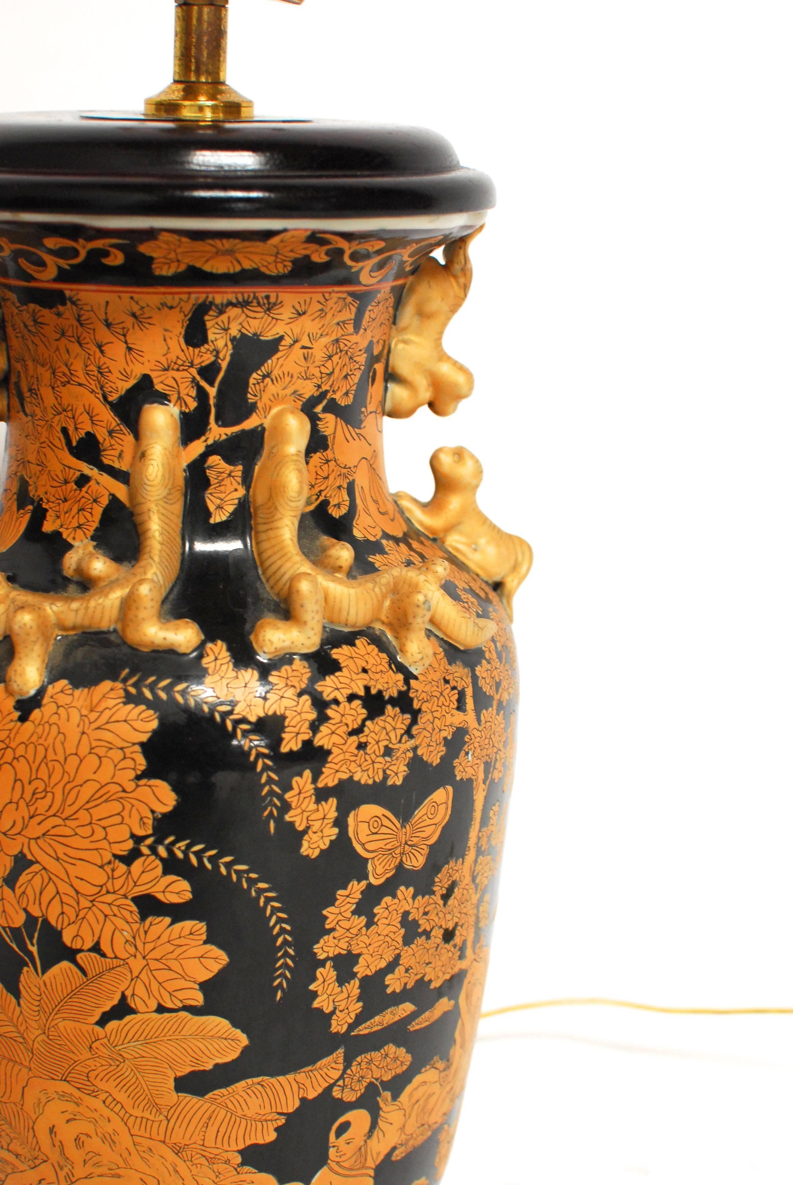 Pair of antique Chinese famille noir vases made of enameled porcelain with applied gilt lizards and figural foo dog handles. Each vase having hand-painted designs depicting young scholars at play amongst temples and trees. Intricate under glazed