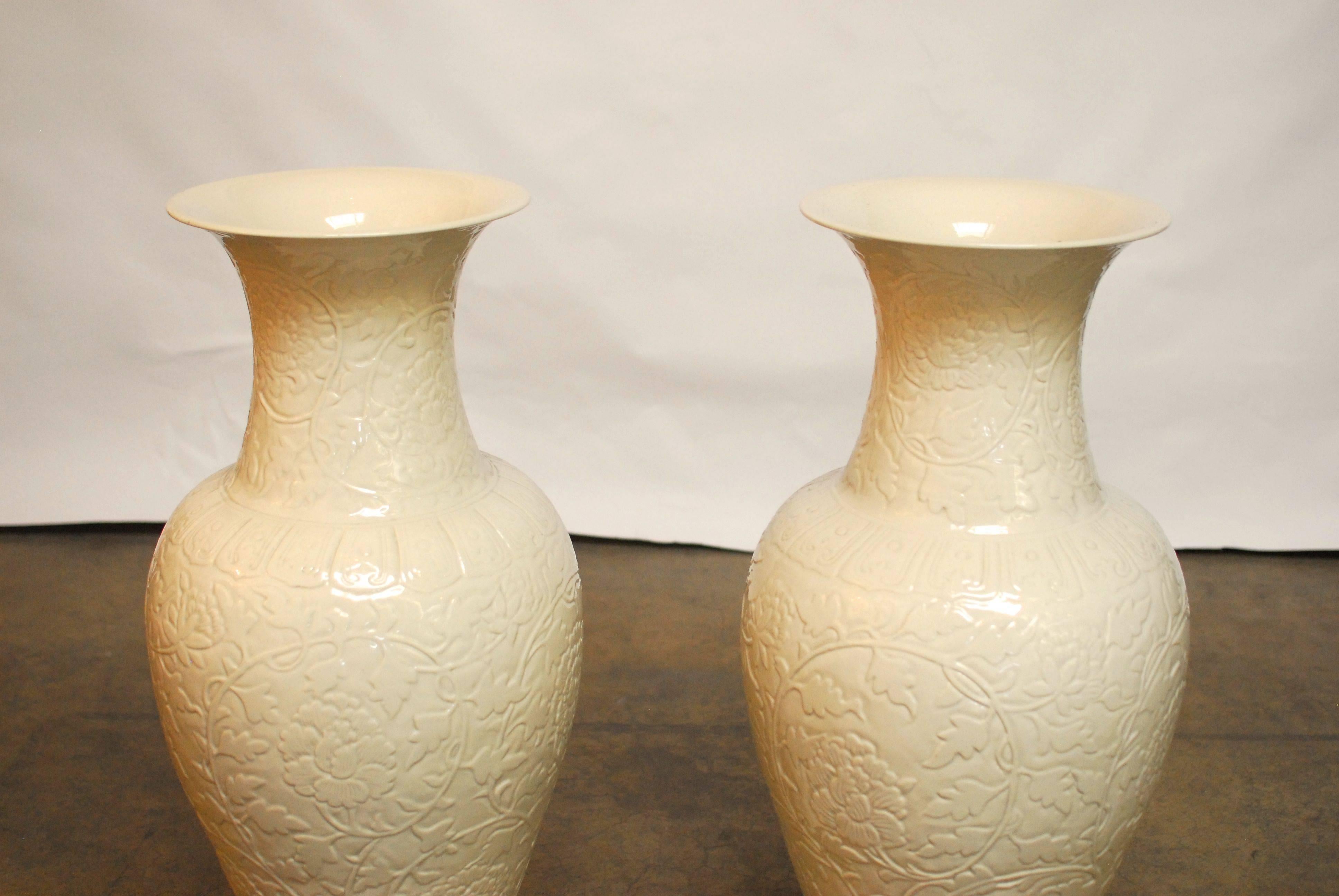 Pair of large, Blanc de chine porcelain vases featuring a trumpet neck and a foliate relief decorated body. Both incised with a flowering chrysanthemum plant on a monochromatic finish.