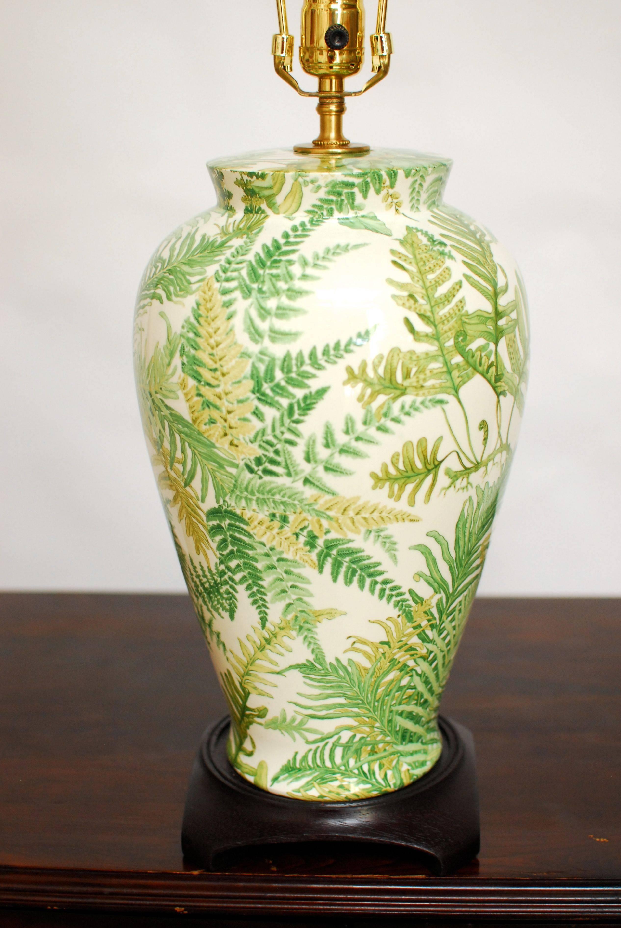 A decalcomania banana leaf ginger jar table lamp decorated with a foliate design. Sits on a carved wood base with an Asian inspired jar form. New brass hardware, harp and finial with no shade. Beautiful pattern with a white background. Purchased