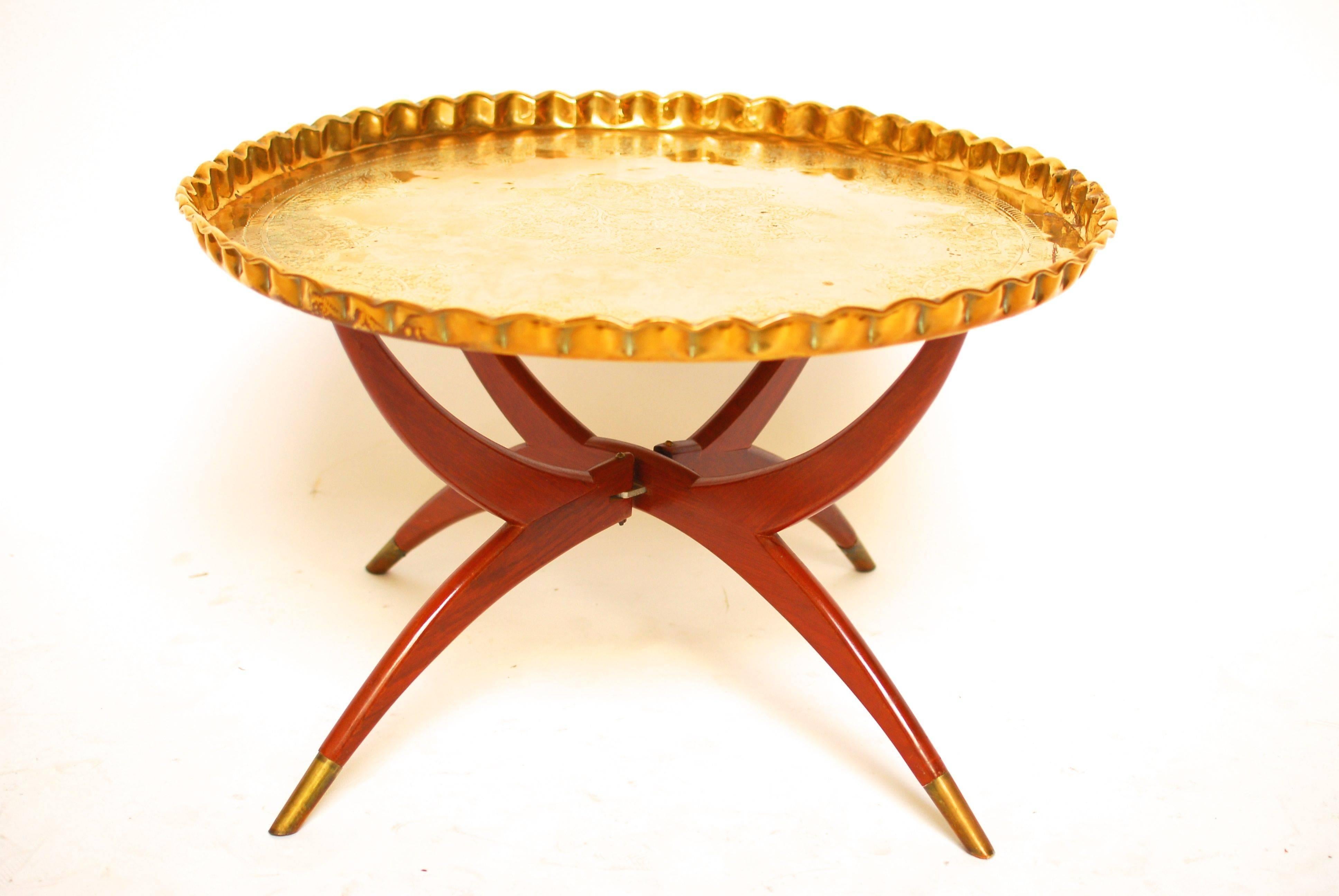 Vintage Middle Eastern engraved brass tray table with mahogany folding Stand and brass feet. The tray is polished and finely carved with foliates and geometric designs. Persian and Moorish style influence the elegance and beauty of this MCM looking