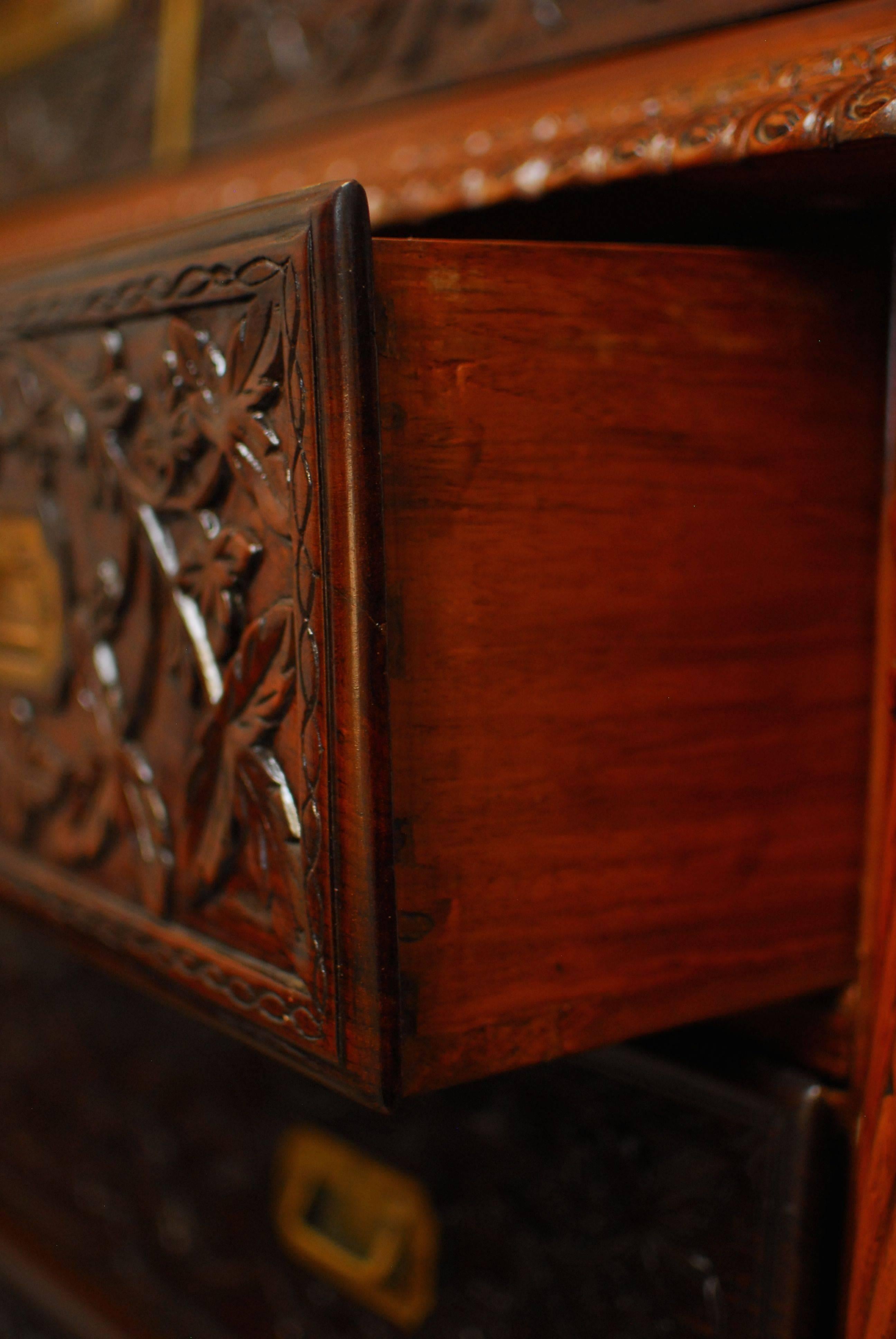Vintage British Colonial library cabinet made of rosewood and teak features intricately carved foliate detail all over the case. Two arched brass trim cathedral windows adorn the top and three large drawers for storage on the bottom. All original