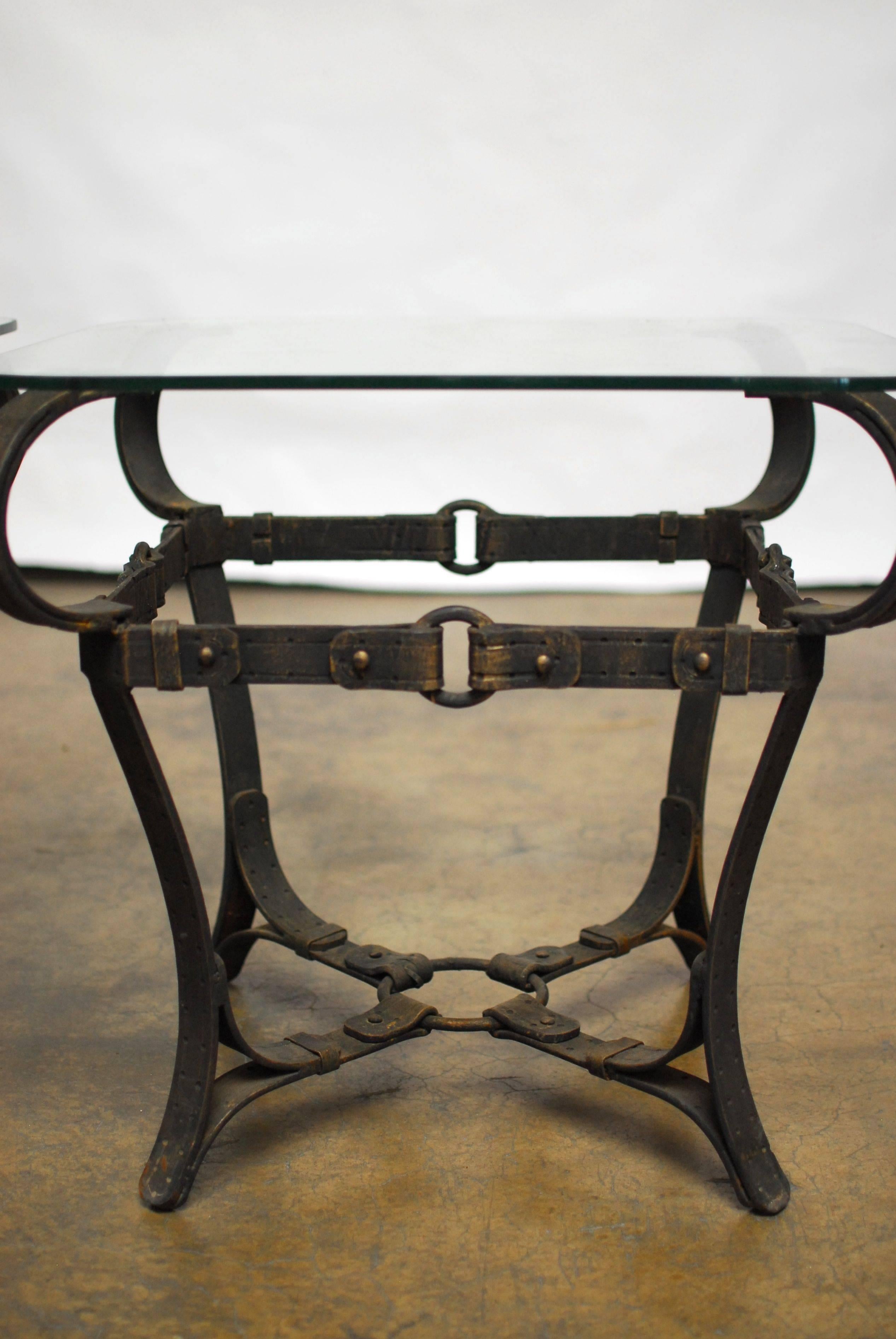 Chic pair of end tables made in the manner of Adnet. Constructed of cast iron faux leather equestrian straps, rings and buckles. With Classic intricate details, vintage patina and a nod to Hermes. Each features a square glass pane with rounded edges.