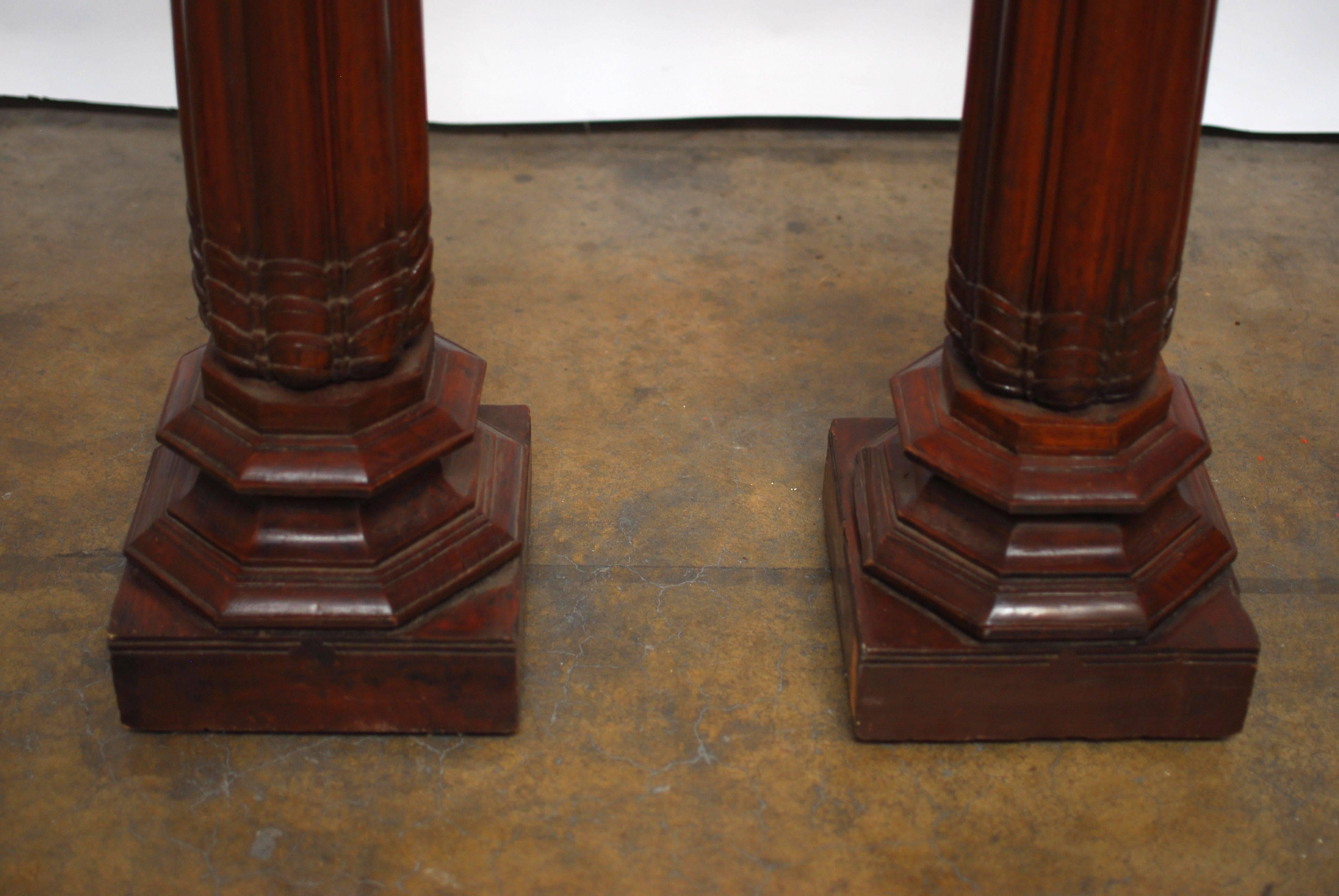 Antique pair of carved architectural columns from Burma made of solid teak wood. Roman style base with a tapered, reeded pillar that terminates with a flat shelf capitol. Finished in a rich mahogany stain. Made in a British Colonial style.
