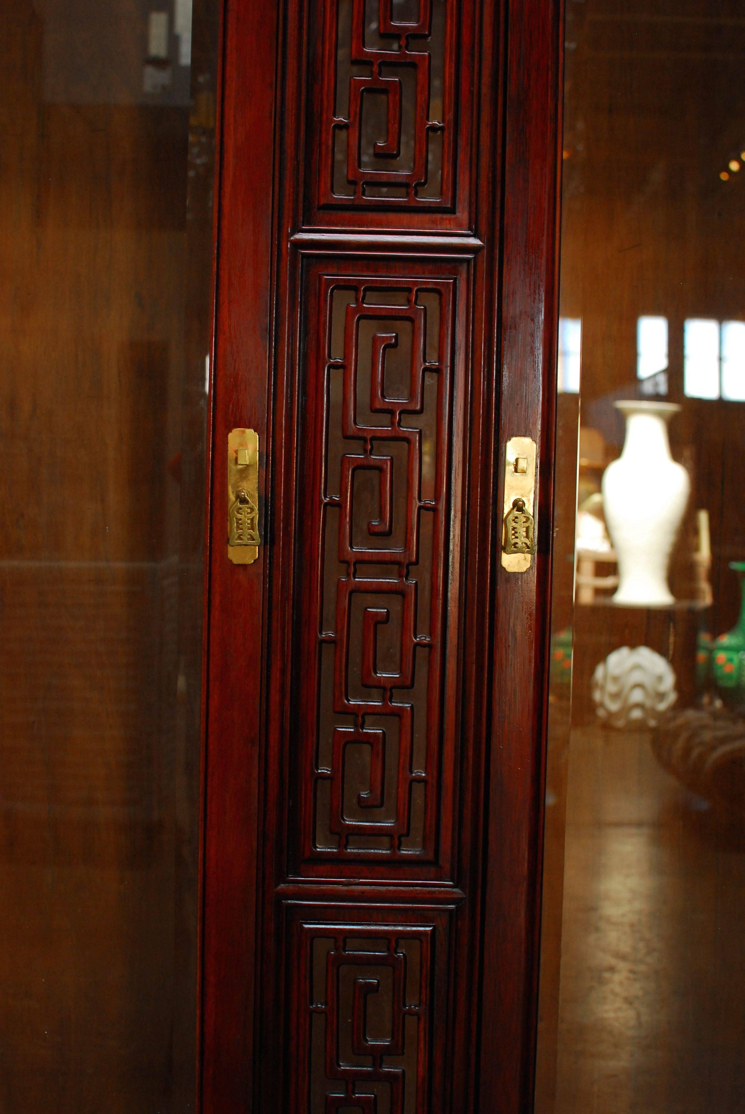 Asian carved rosewood display cabinet with Greek key decorated cornice and front panel. Two large front doors with beveled glass and brass lock plates. Interior has four adjustable glass shelves and beveled glass on each side of the case. The