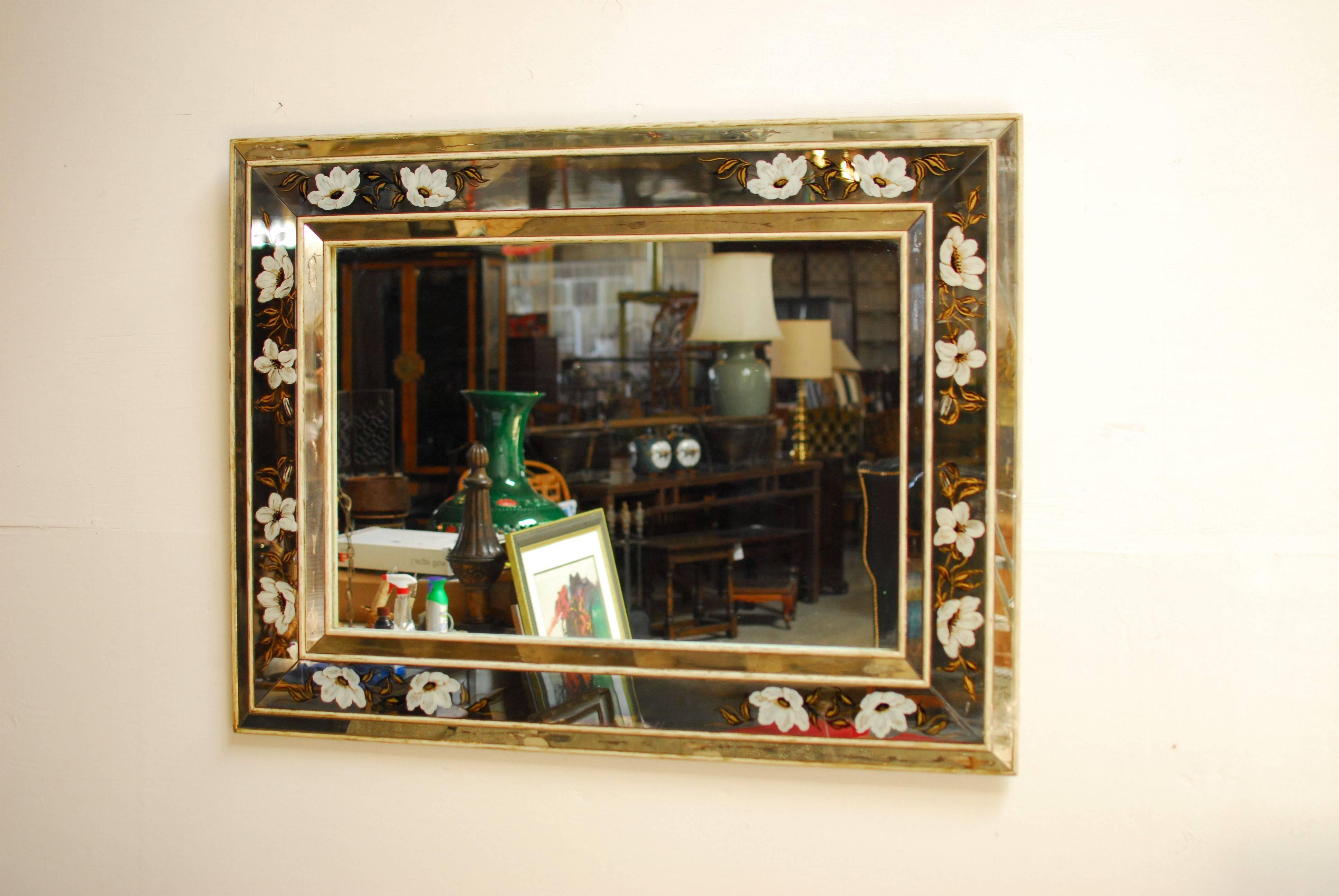 Large, antique French reverse painted églomisé mirror decorated with white poppies and foliate detail in gilt. Bordered on the inside and outside perimeter with angled glass. The painted mirror and glass are separated by a handsome wood trim.