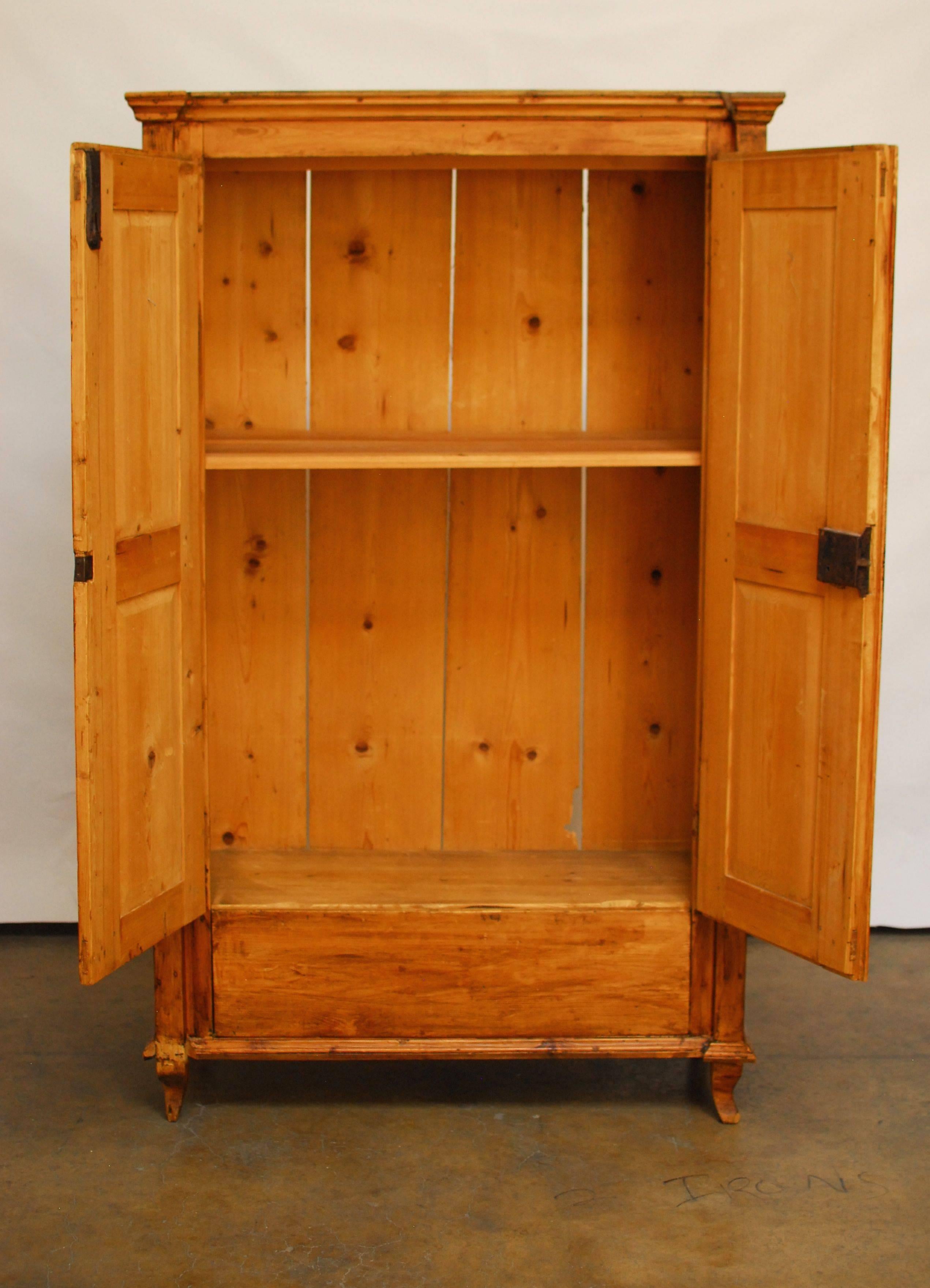 A rustic 19th century French country pine armoire with decorative carved side columns that extend to the top molding. Period correct hardware and lock plates. Made with wood peg joinery and hand dove tail construction bottom storage drawer. Sits on