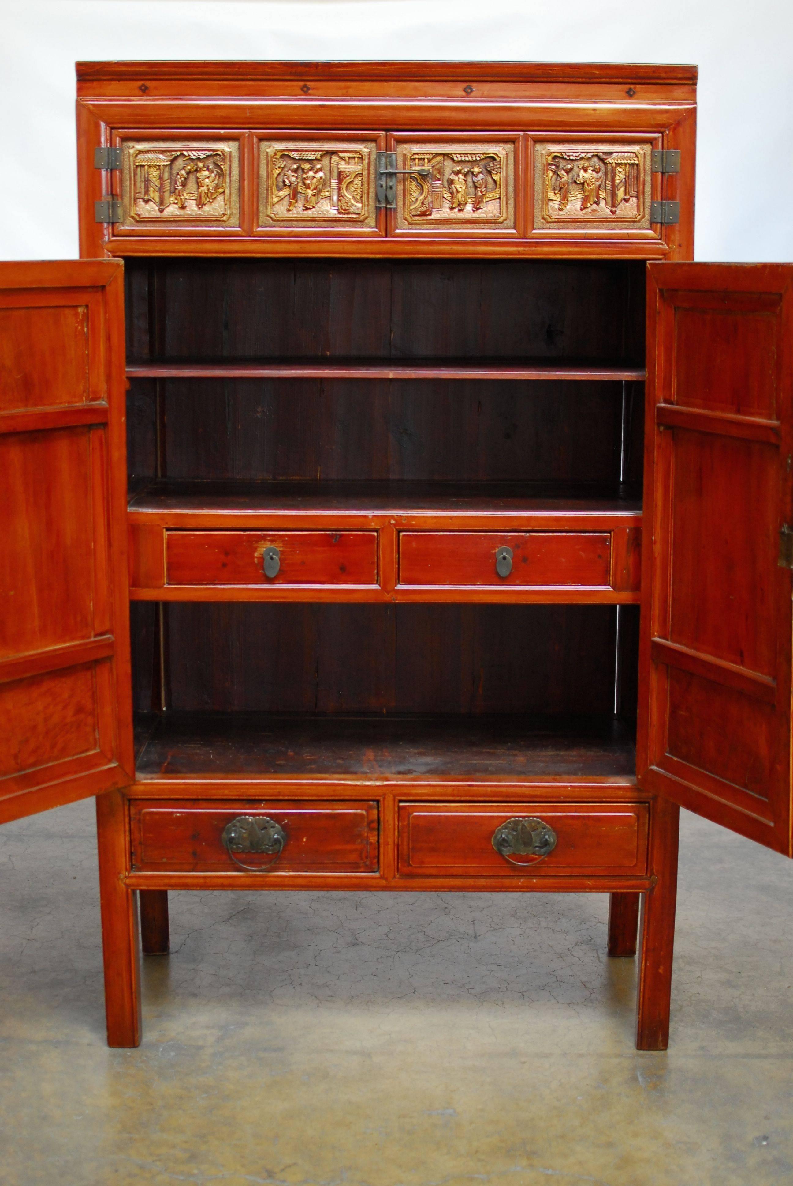 Chinese export cabinet with two large decorated doors carved and finished in black lacquer and gilt trim. Two small doors on top decorated with carved social scenes and adorned with gilt trim. Interior has three large shelves and is fronted by two