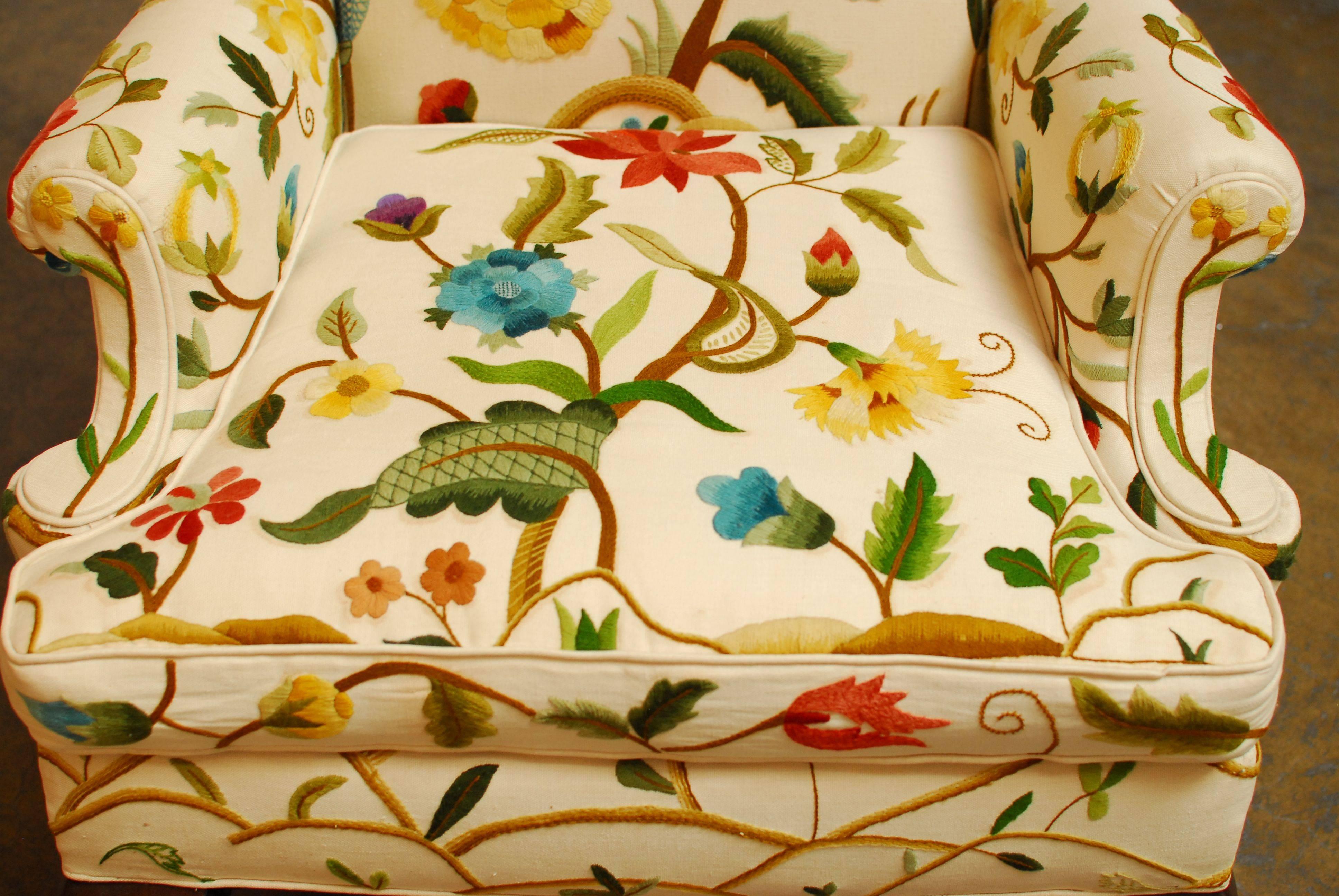 Vibrant floral crewel work upholstered wingback chair made in the George III style with cabriole legs and turned stretchers. The upholstered linen features bright shades of red, blue, yellow, and green flowers and butterflies finished on all sides.