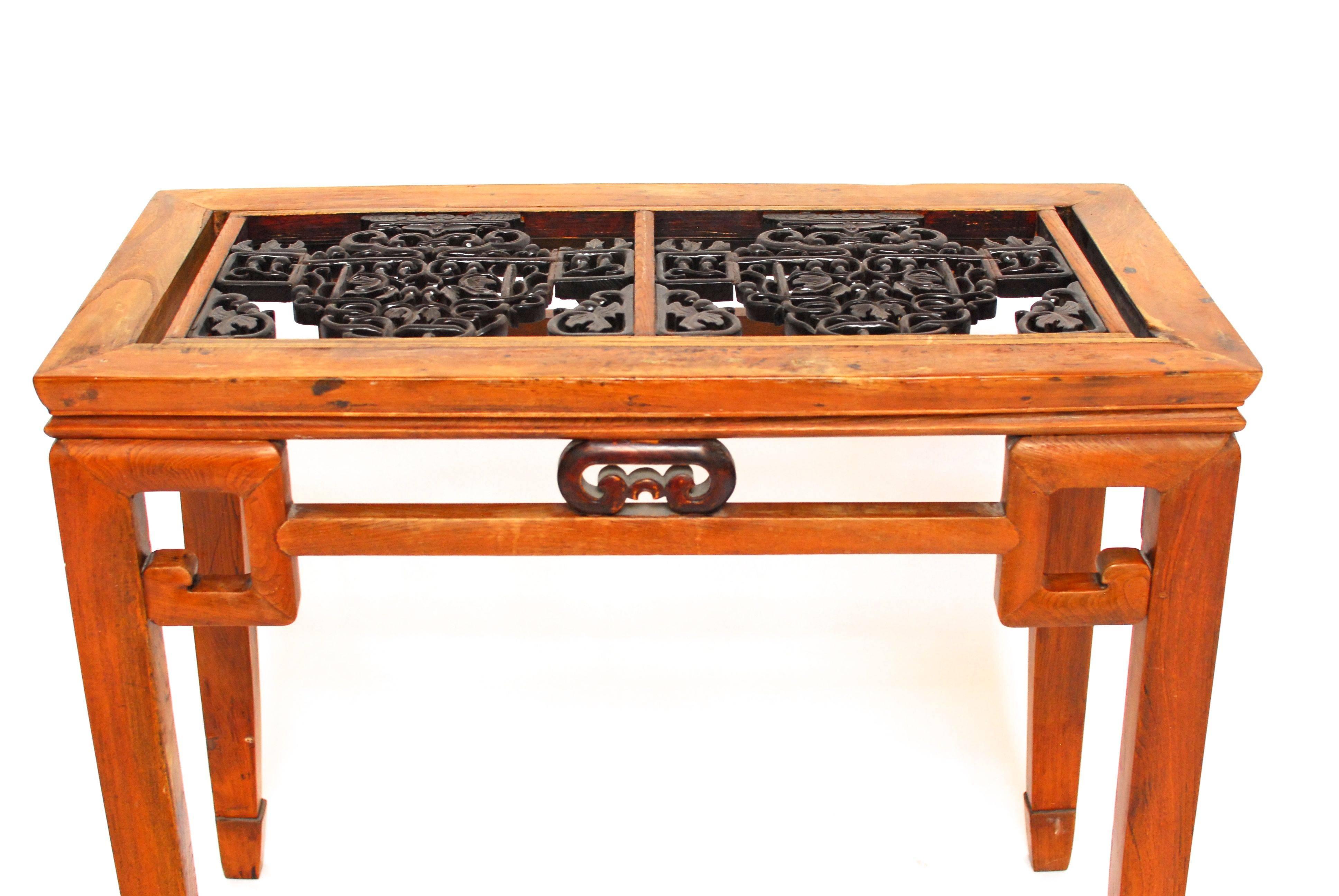 Unique Chinese hardwood carved Greek key entry table with an ornate window panel inlay. It sits on square legs with Greek key shaped details and straight stretchers, standing on subtle horse feet. The window panel has an intricate carving with a
