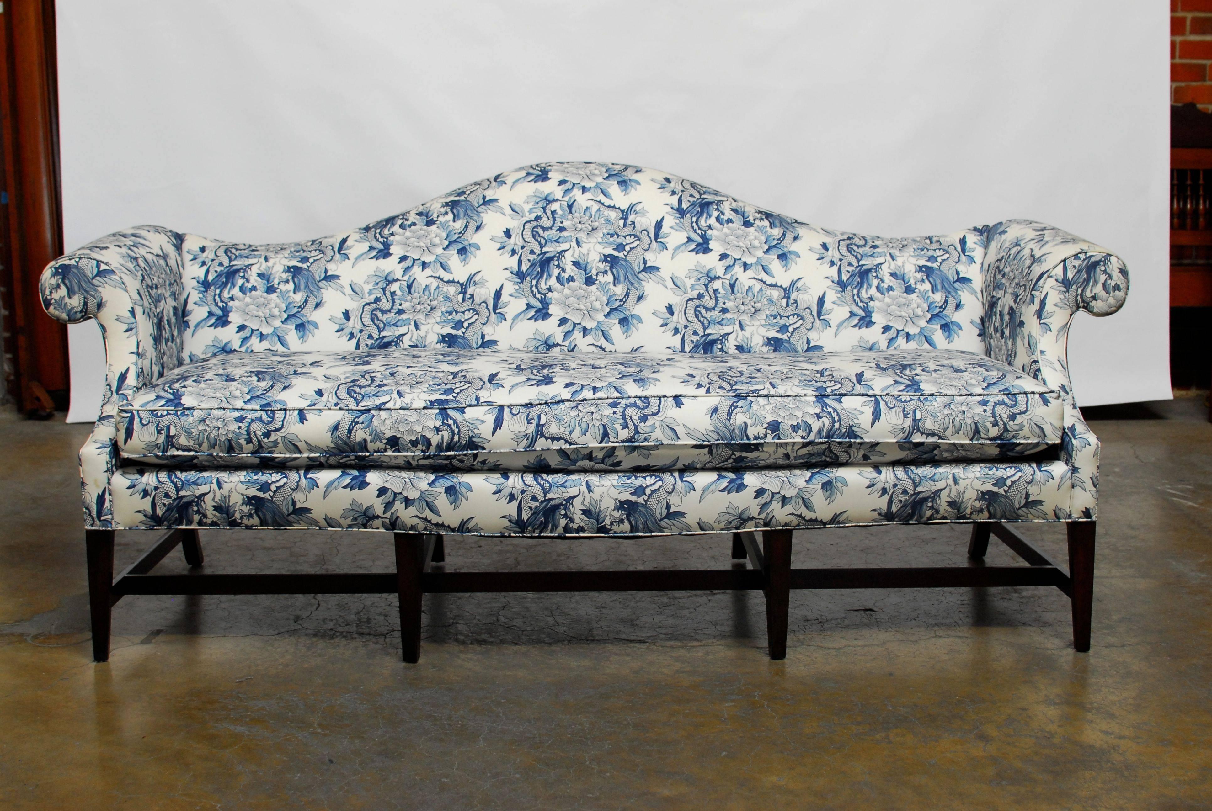 Dramatic Chippendale style sofa with a camelback form and a serpentine bow front edge. Features Ralph Lauren toile chinoiserie style blue and white upholstery with dragon and foliate detail. Sits on four tapered front legs with cross stretchers and