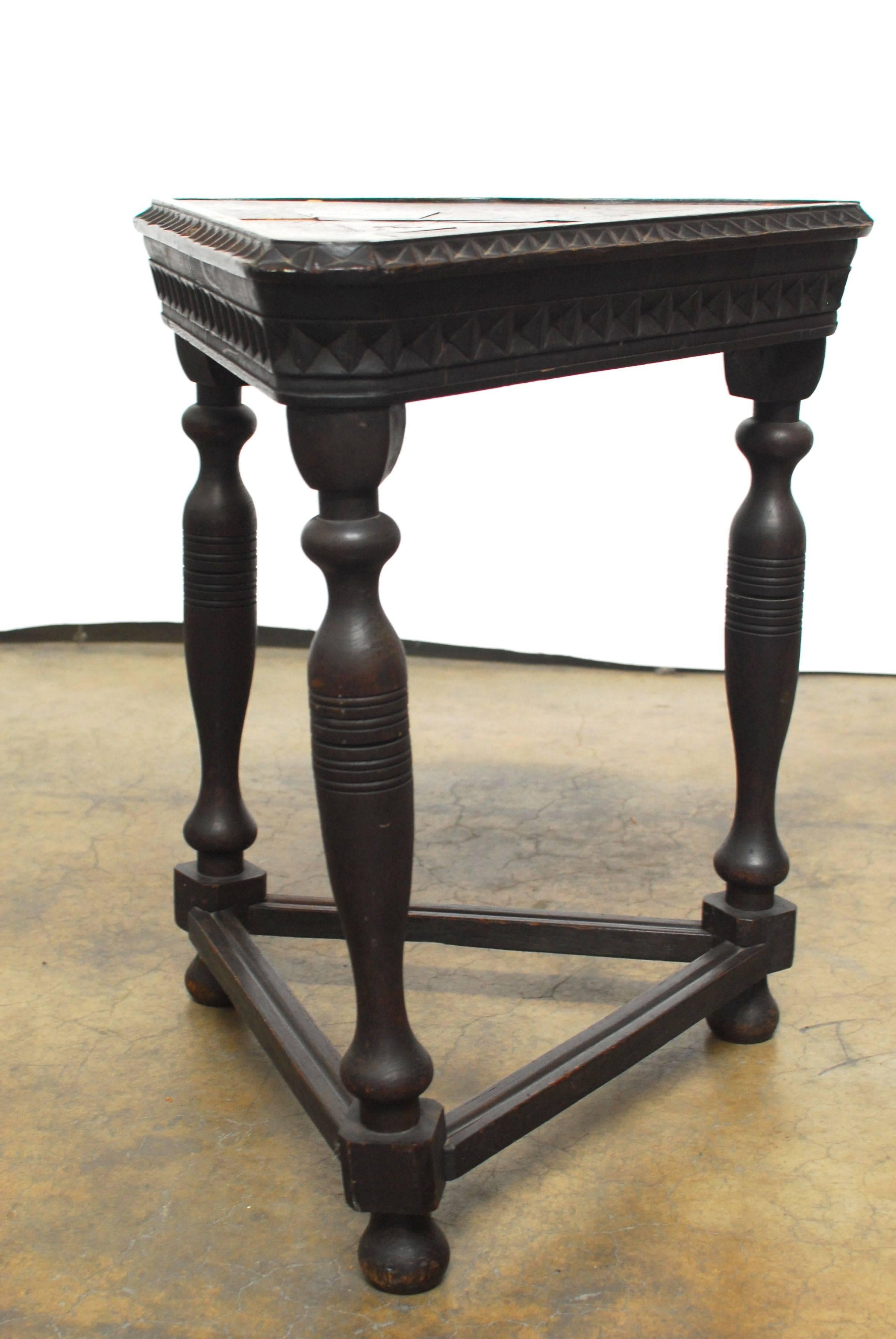 Unique carved triangular table with 3 turned legs and featuring a heart shaped top with geometric design carved apron, and a geometric inlay top with a cross motif. Square box stretchers with round feet. Carved oak has a ebonized finish.