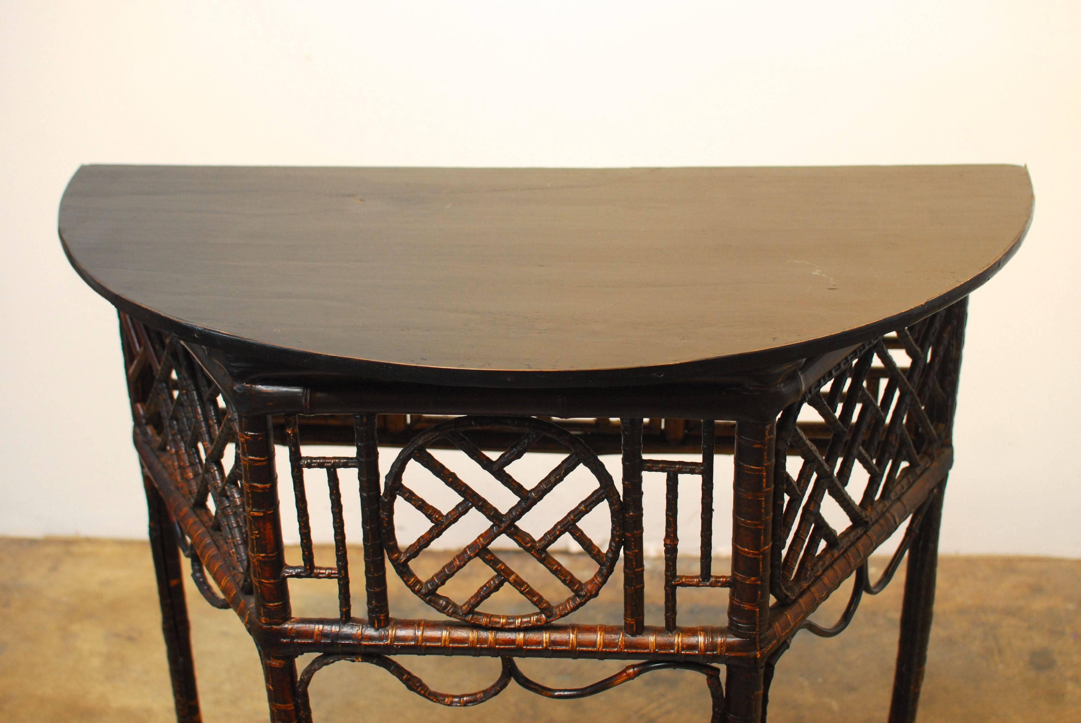 Elegant Chinese bamboo table with a 4 sided geometric fretwork design and a demilune shaped black lacquer wooden top. Delicate bamboo trim and bamboo spreaders. Would make a great entry table or console table.