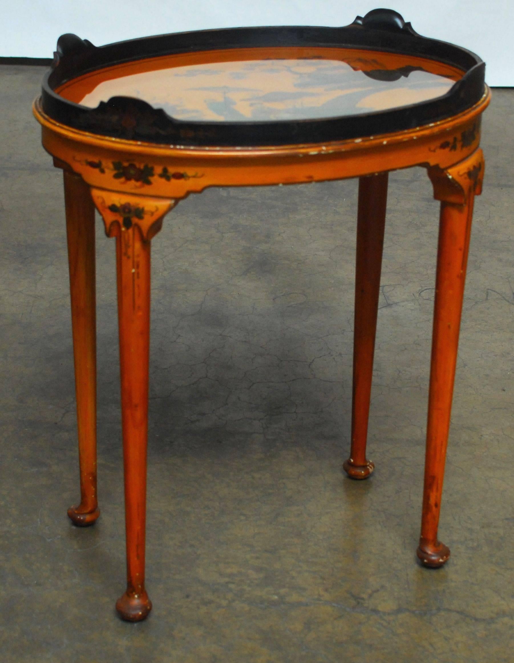 Rare, Queen Anne style oval tea table featuring a removable glass tray top and chinoiserie decoration. Finished in a warm faded orange lacquer sitting on long, tapered legs with pad feet. Floral painted detail on tray, apron and legs.
  