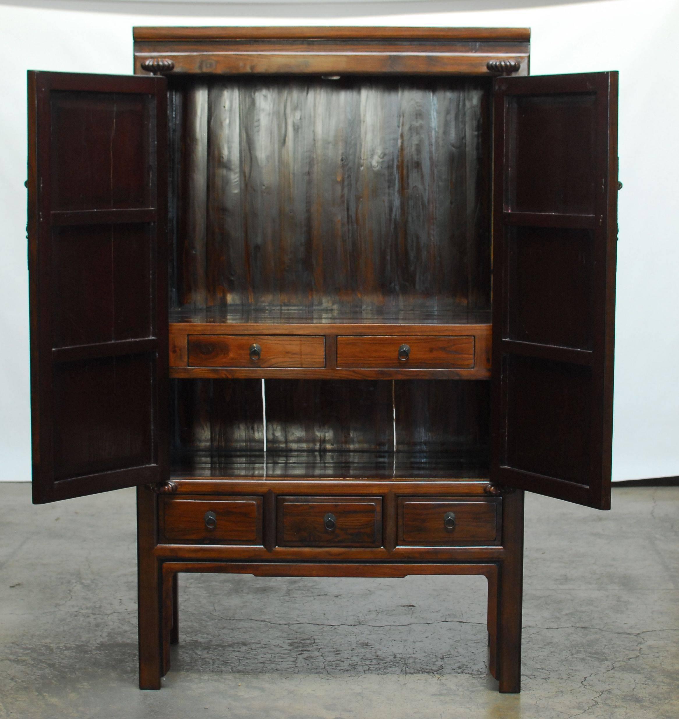 Handsome Chinese kitchen cabinet armoire fronted by two large doors with wooden hinges. The doors open to reveal a large storage area centered by two drawers. The cabinet is finished in a dark lacquer. Rising on square legs with shaped aprons and