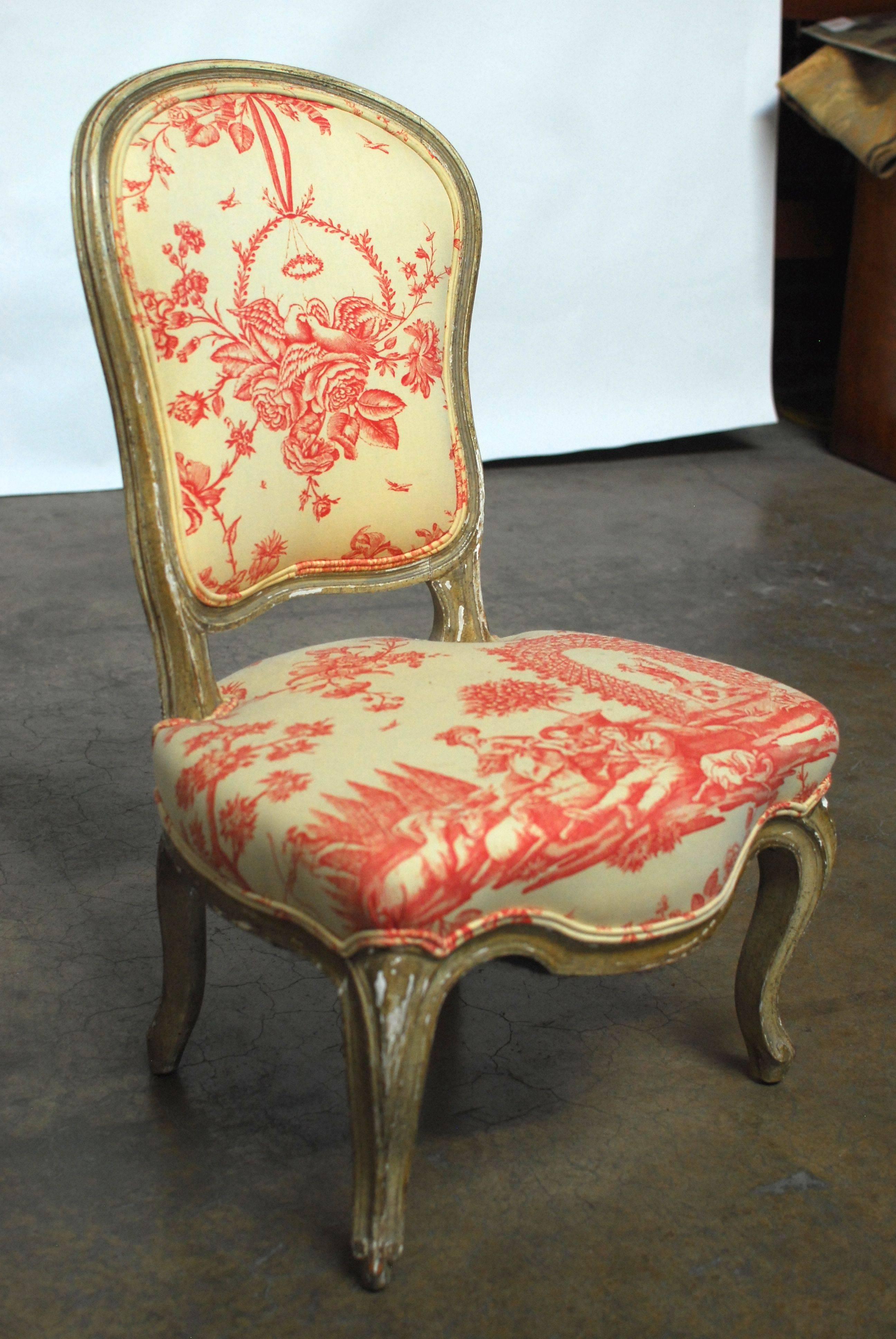 French Louis XV style slipper or boudoir chair featuring a serpentine carved frame and cabriole legs. Upholstered in a red and cream toile fabric with a double welt border. Frame has original unrestored finish and tight joinery. From the Pebble