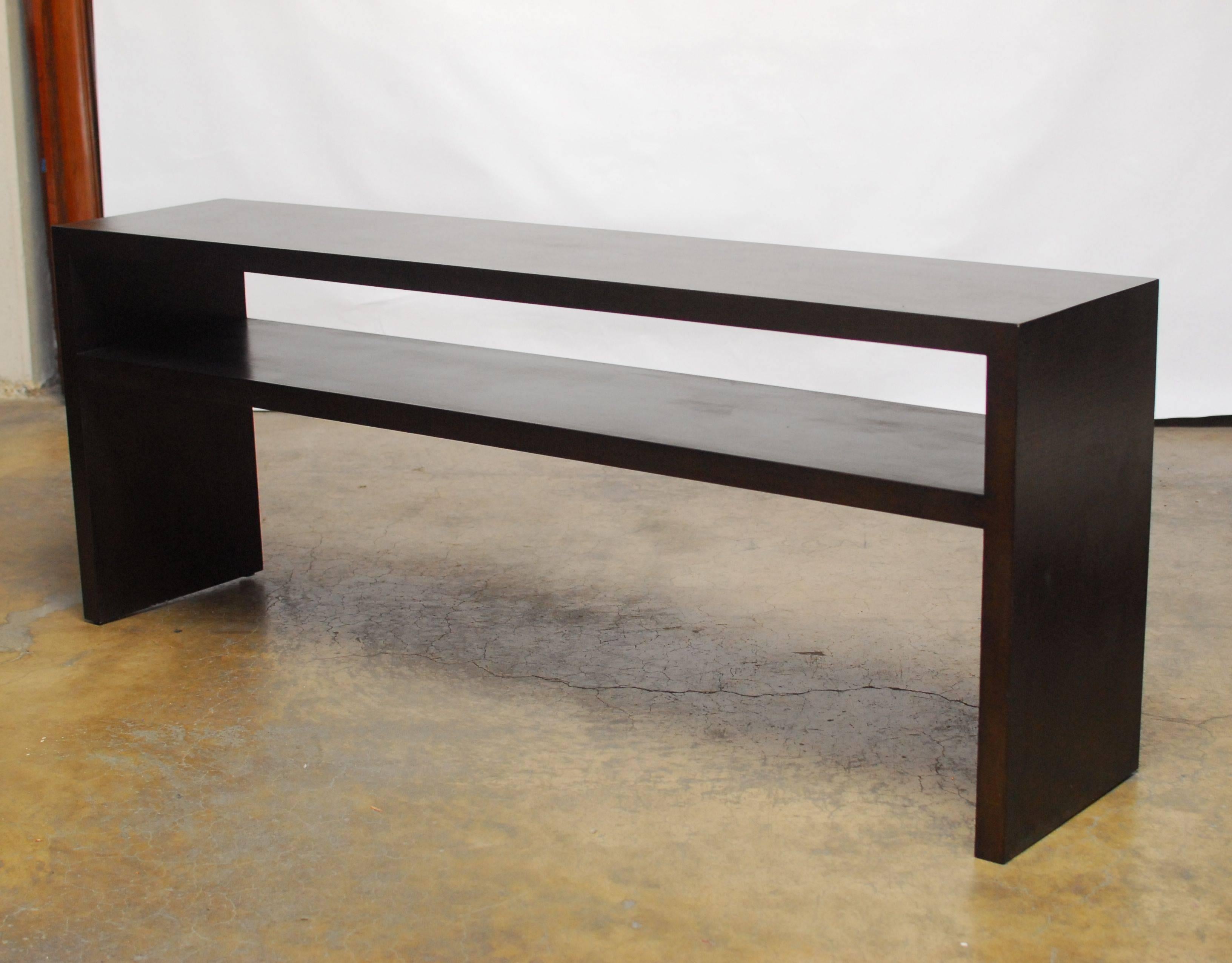 Large, Modern Parson's style console table with a shelf featuring a sleek, minimalist style and covered with a distinctive textured grasscloth veneer. Extra long sofa table features a wooden frame and is finished is rich, dark espresso.

