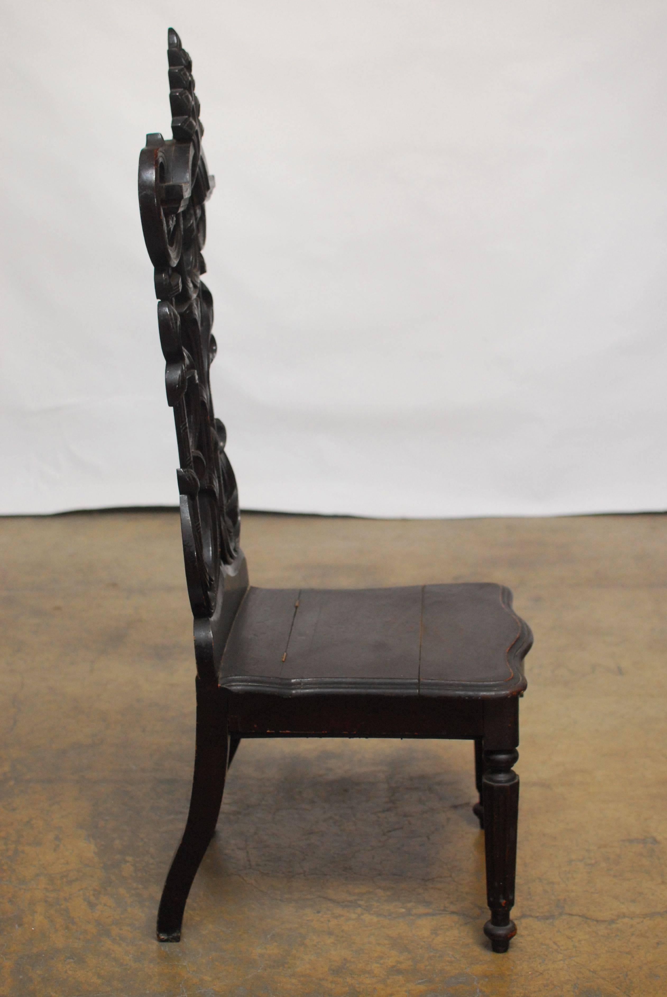 German hall chair made in the Rococo style with an ebonized finish. Elaborately carved pillared back with decorative "s" scrolls and an acanthus finial crest. The plank seat is hinged and opens to a small storage space. The chair sits on