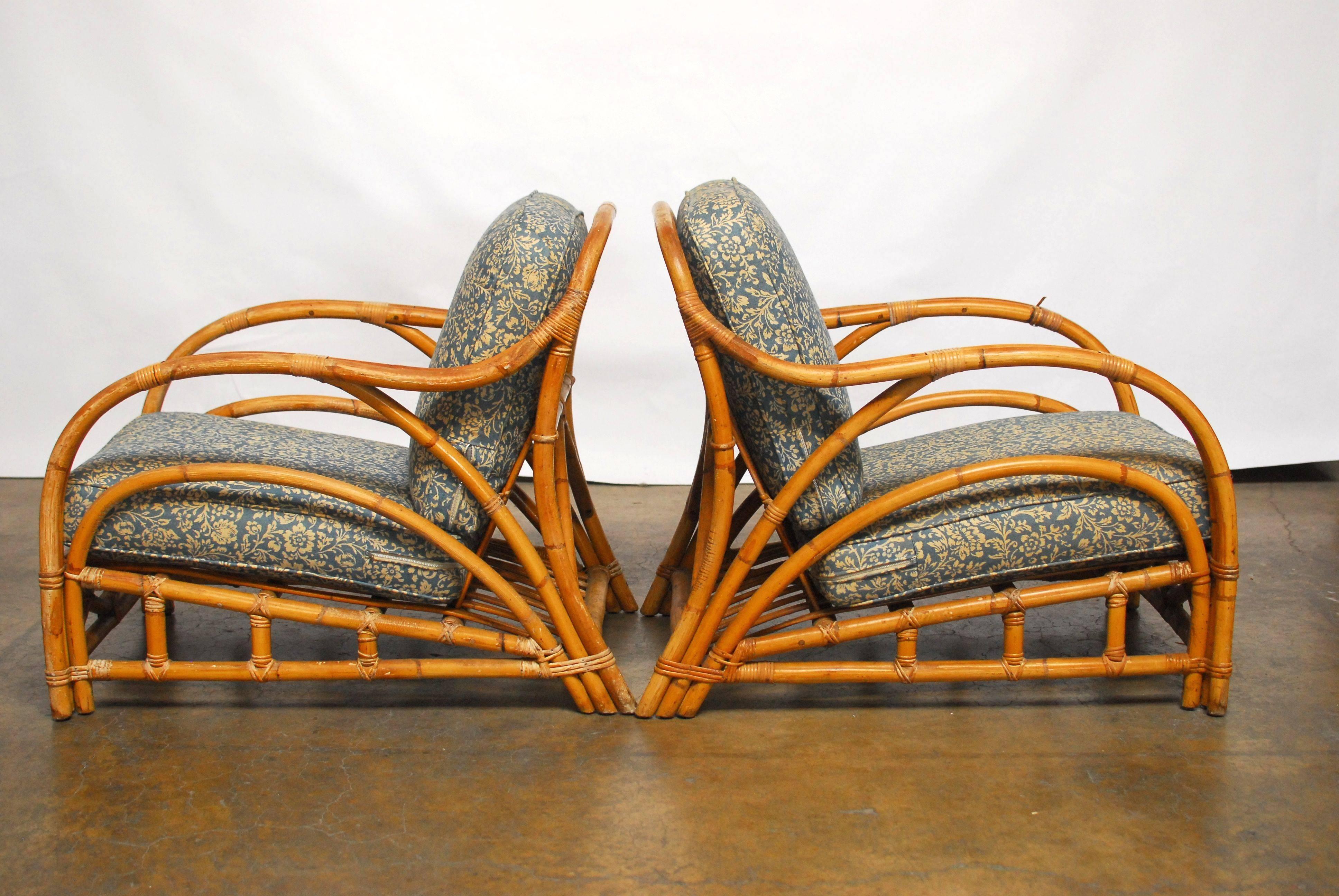 Pair of chic, Art Deco style bamboo lounge chairs with original condition upholstered cushions with a foliate pattern. Featuring a low slung seat and long, graceful curved arms. Includes a rattan ottoman foot stool. Rare design with complex aprons
