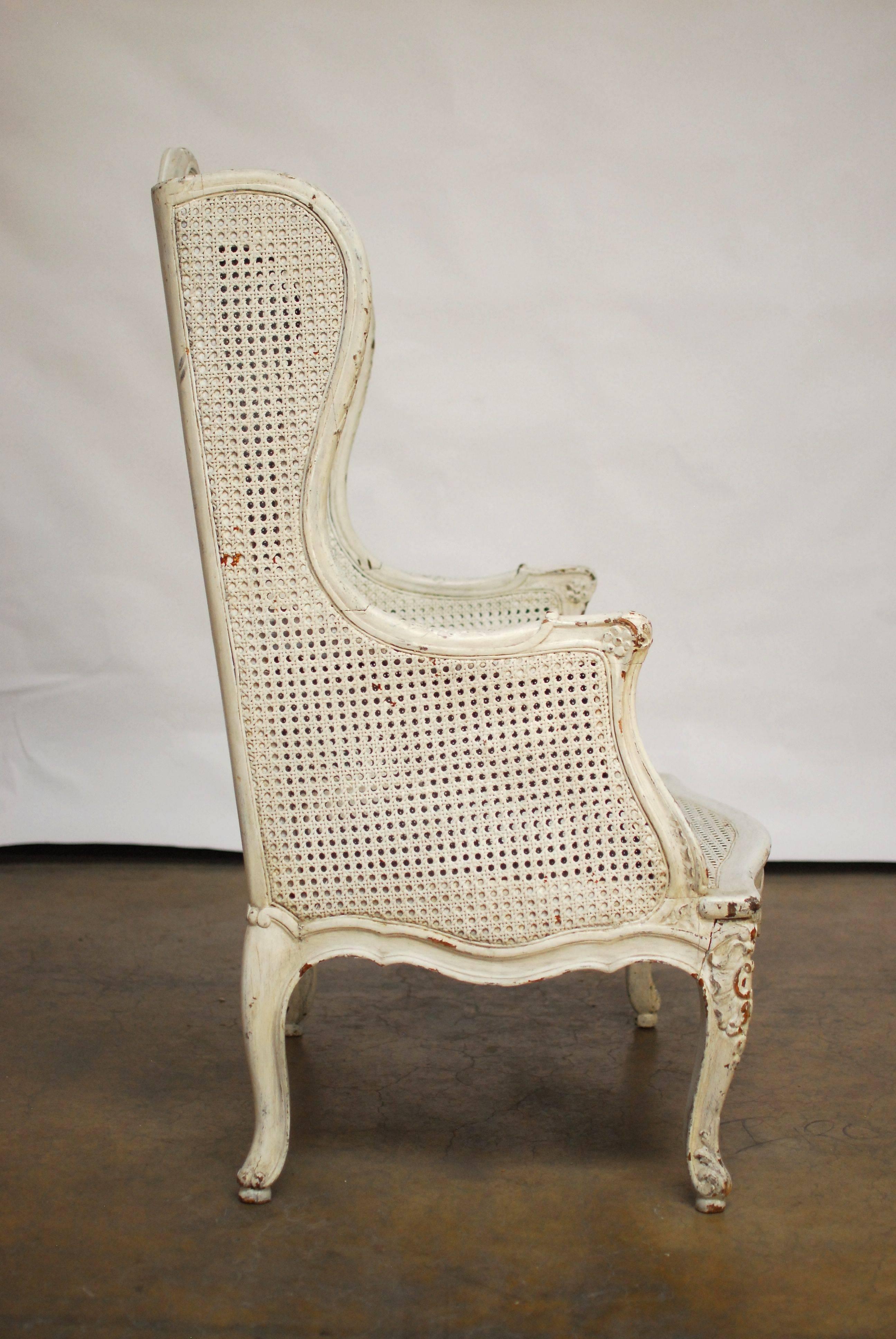 Rare antique French Louis XV style wingback bergere featuring cane sides, back, and seat. The sides having double cane and a hand-carved frame with cabriole legs. Rich with intricate carved details and small losses to original cane. The chair has