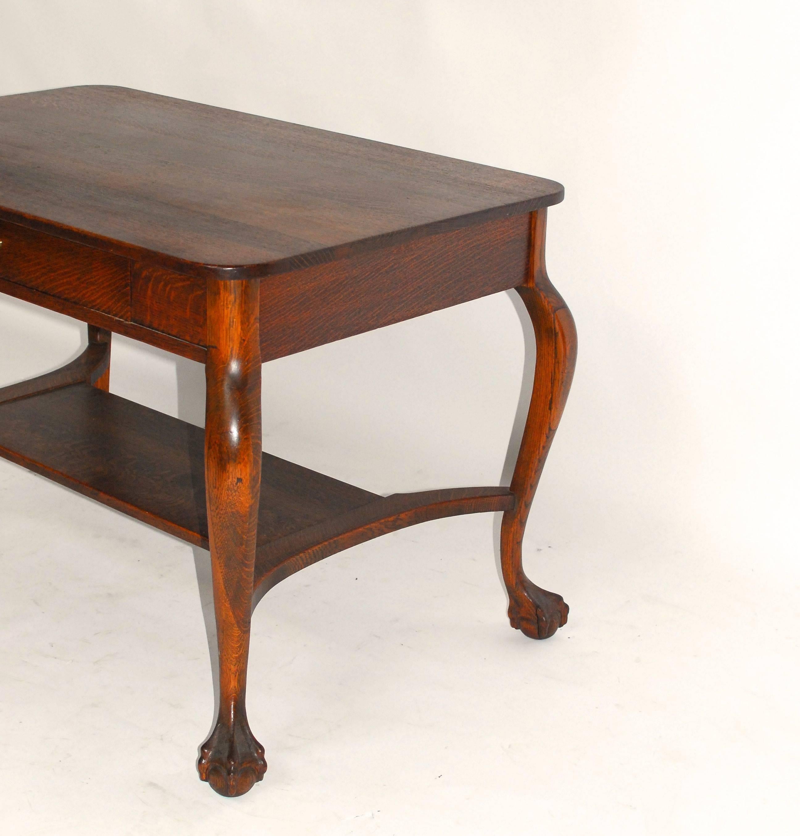 Chippendale style oak library table desk with quarter-sawn panels and delicate, carved cabriole legs with ball and claw feet. It's fronted by one large drawer with a brass metal pull. This elegant writing table also features a stretchered bottom