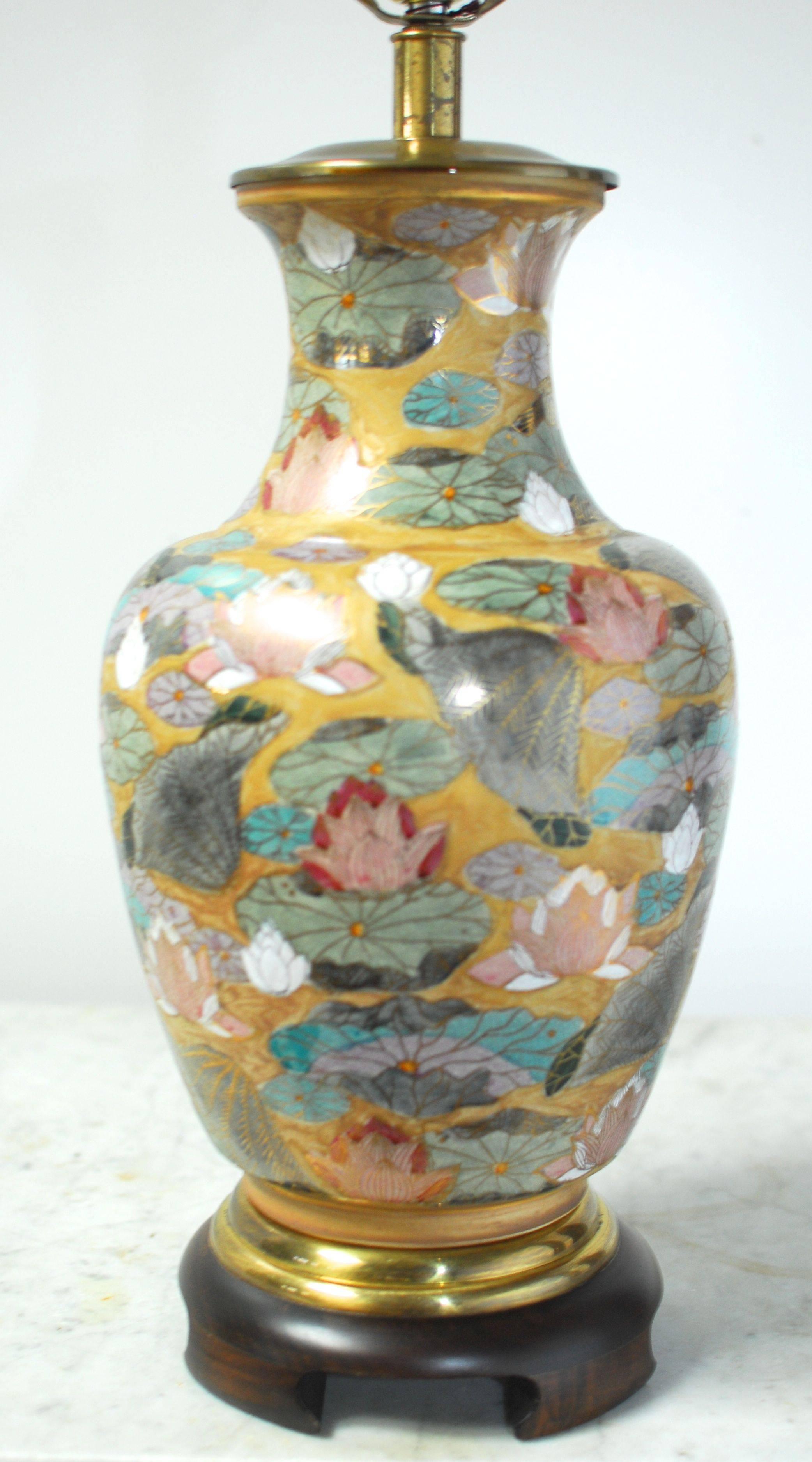 Asian style ginger jar form table lamp by Frederick Cooper of Chicago featuring a hand-painted gold leaf decorated vase with a colorful floral motif. Stands on a carved wooden base with a brass stand and brass hardware and lid. Includes an Asian