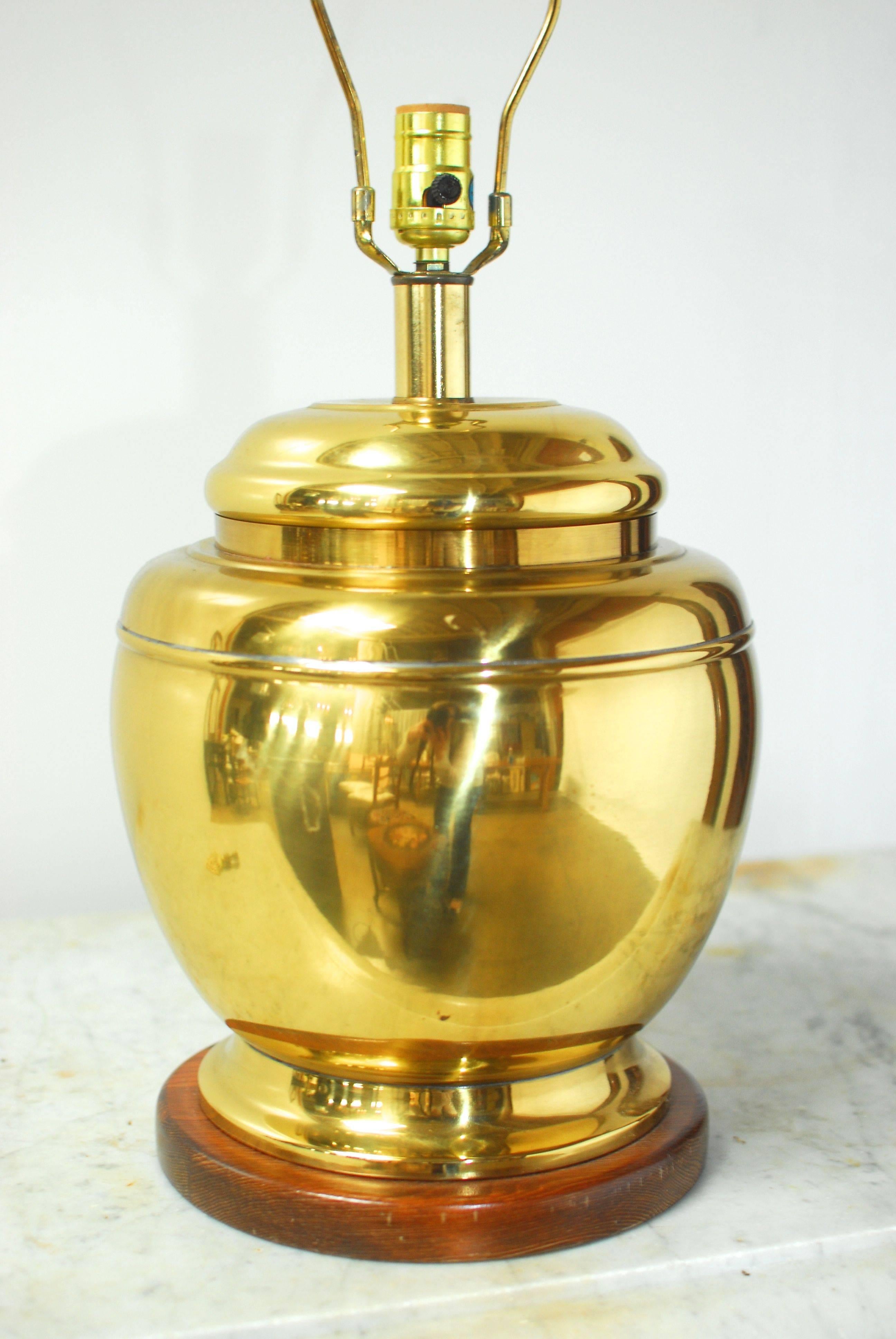 Hollywood Regency style brass table lamp with a lidded jar form made in an Asian style. Attributed to Frederick Cooper of Chicago. This table lamp sits on a wooden plinth and includes a harp and finial and no shade. Unique urn shape with a