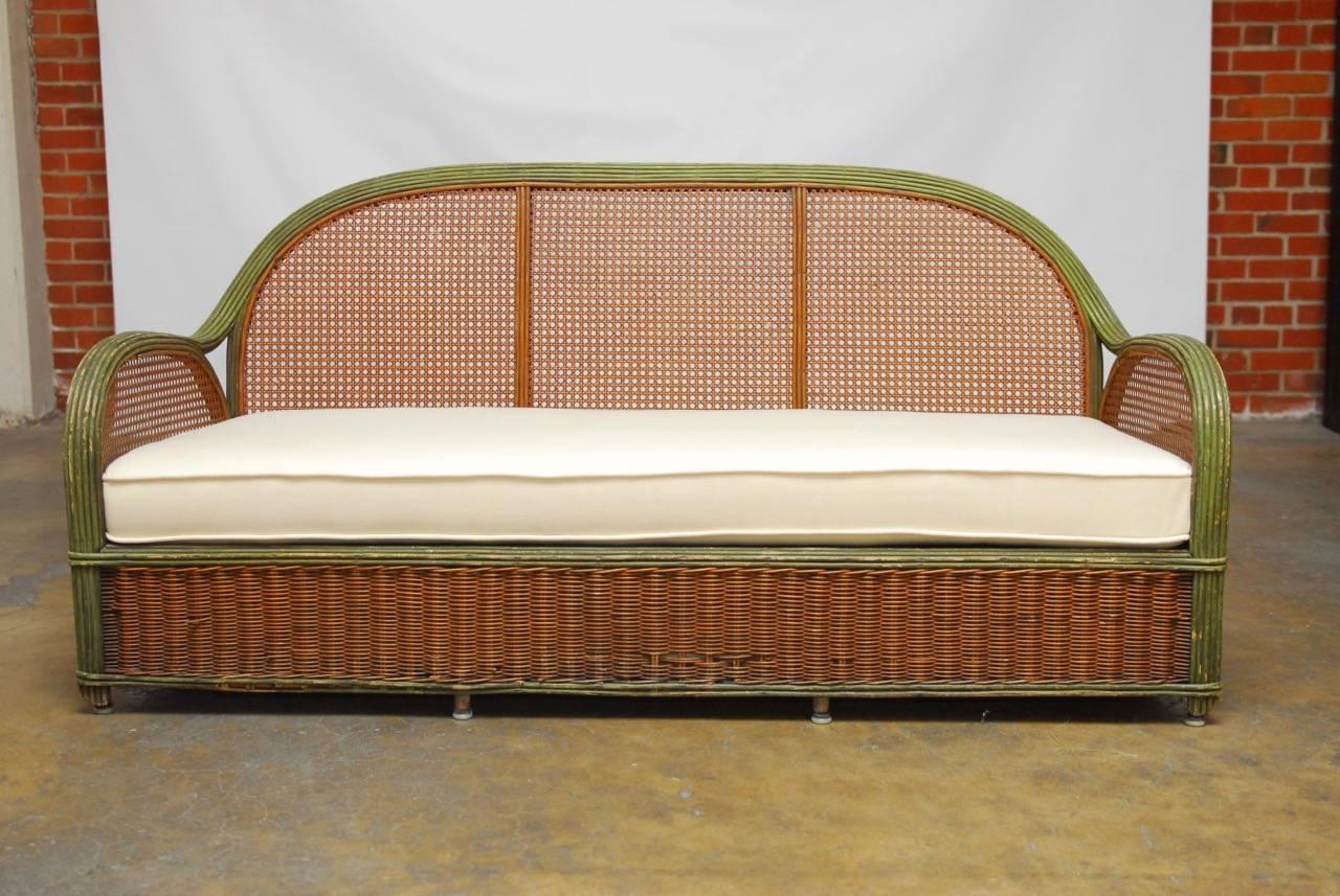 Fabulous French Art Deco settee constructed with a wooden frame and long graceful rattan arms that curve up to the humpback crest. The bottom of the frame is covered in wicker and the sides and back are finished in cane. Rattan arms and back are